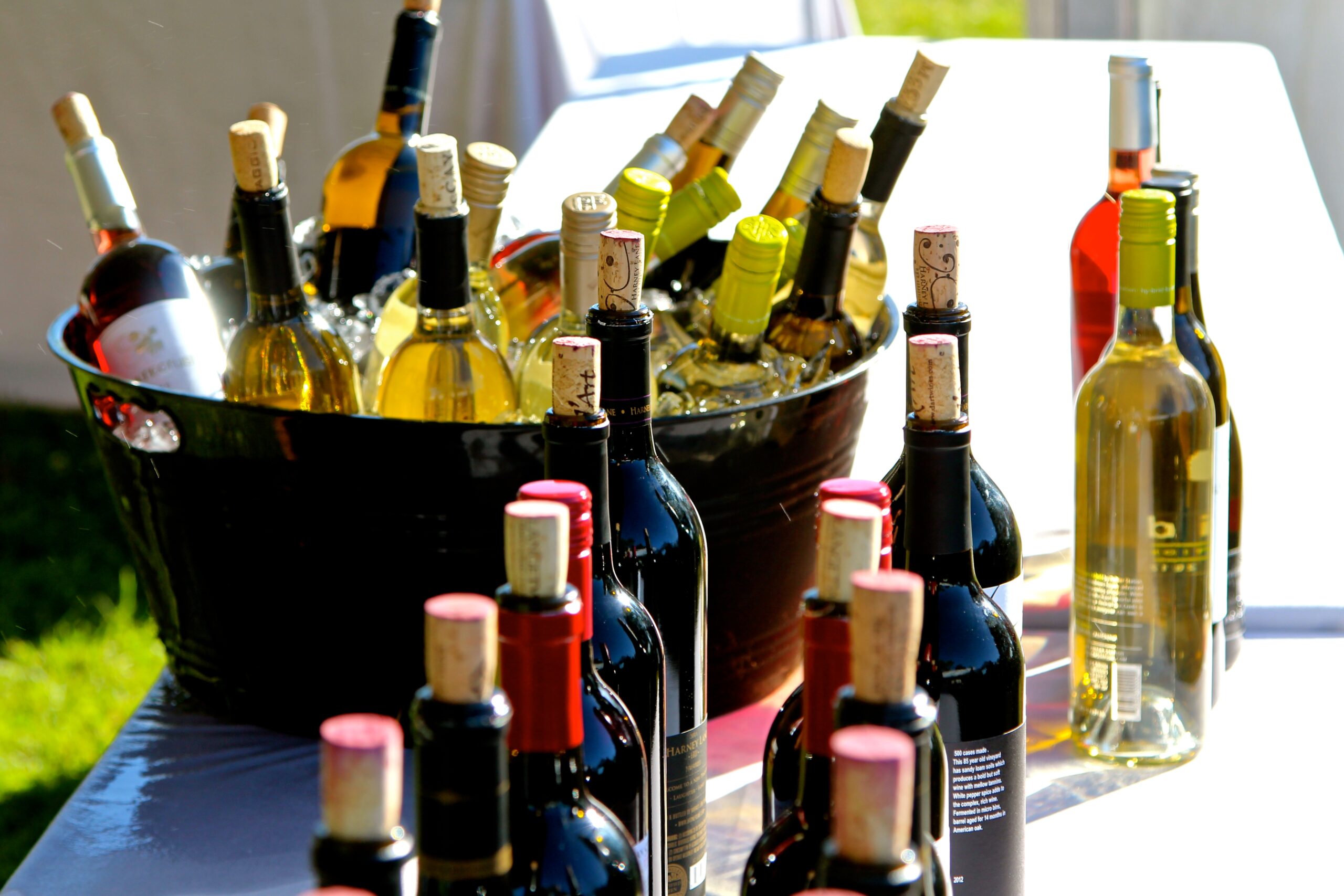 Assorted wine bottles with corks in a black bucket on a table outdoors, promoting Lodi wine region.