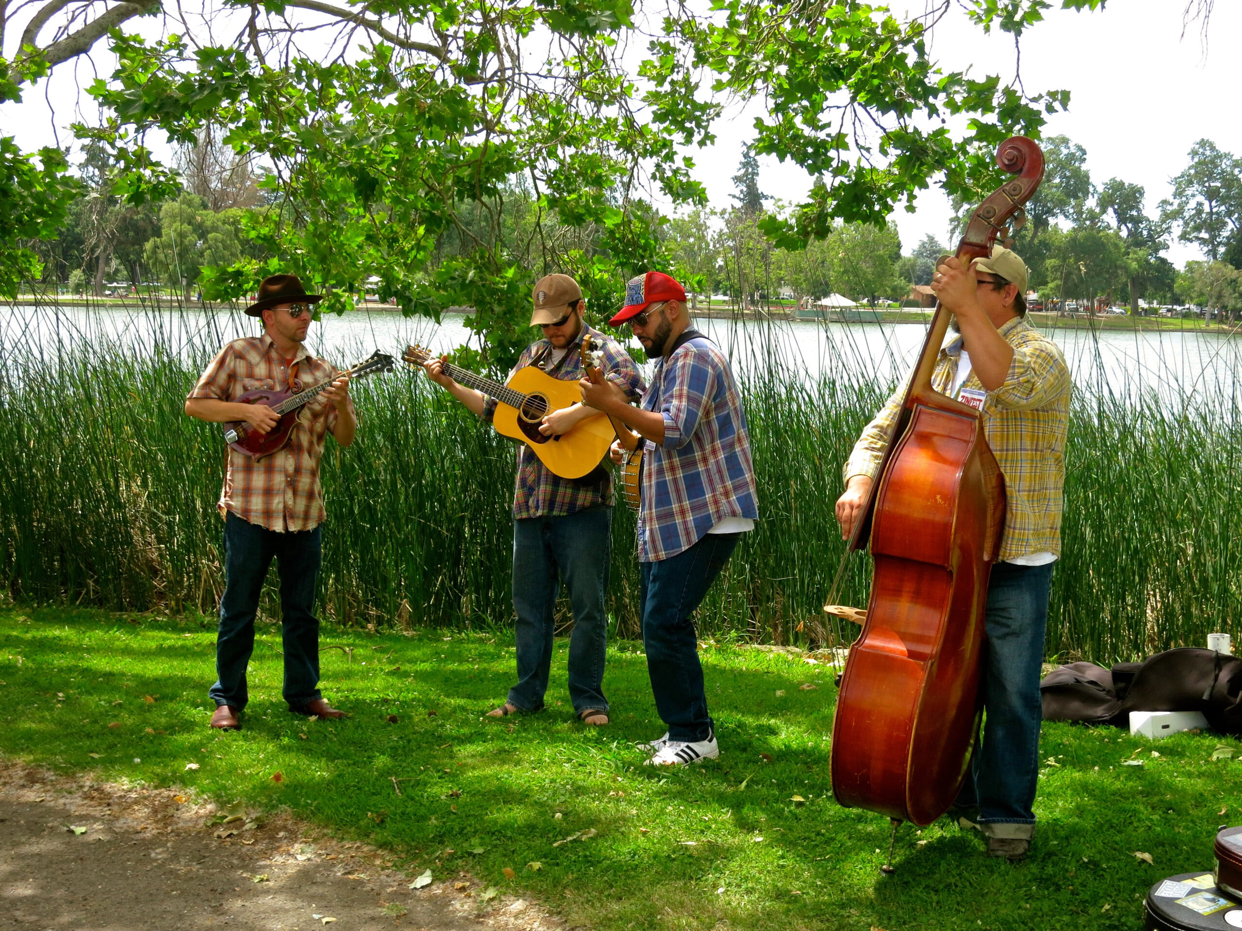 Musicians playing guitars and double bass outdoors near a lake in Lodi, California.