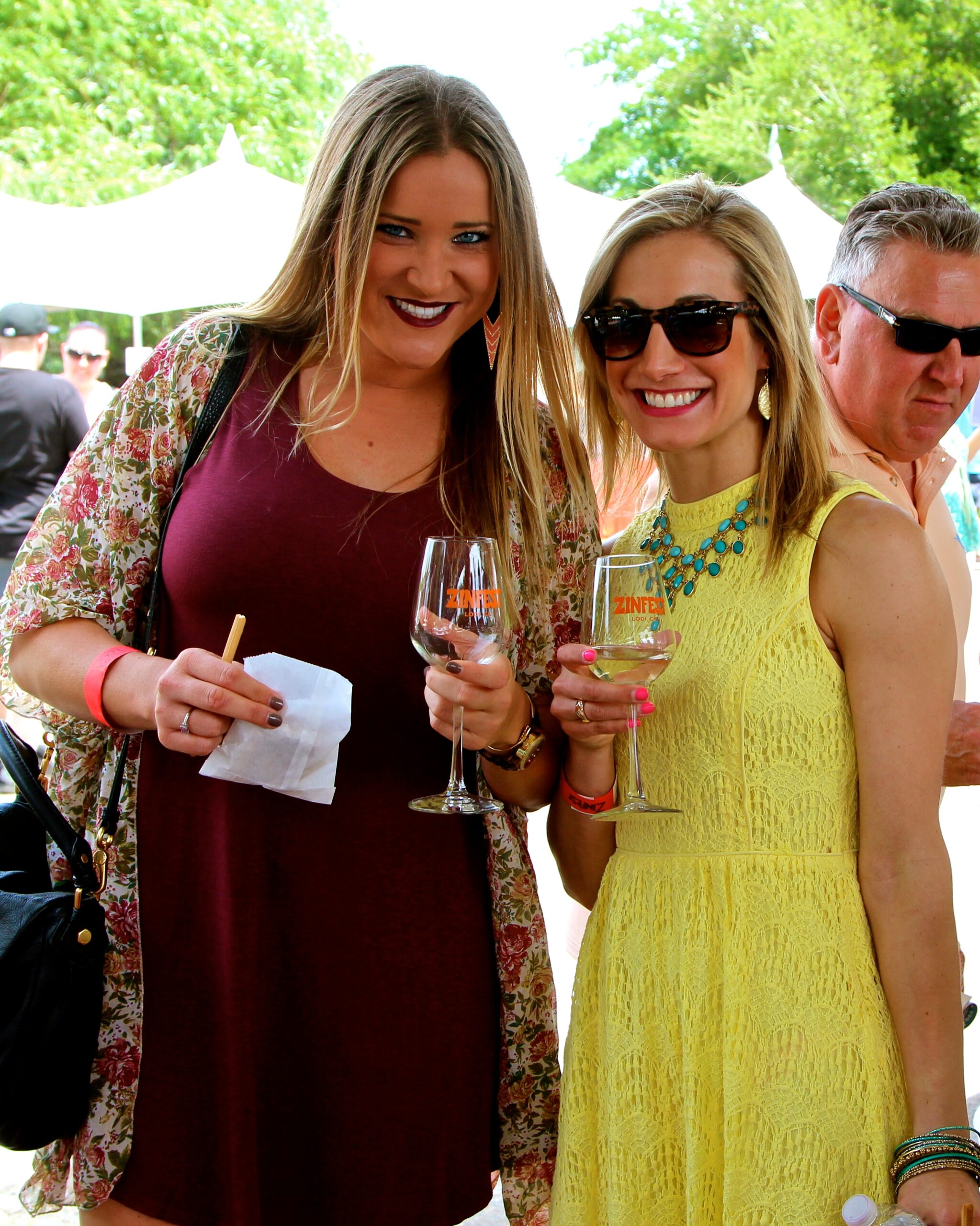 Two women enjoying wine at a Lodi Winegrape Commission outdoor event in sunny weather.