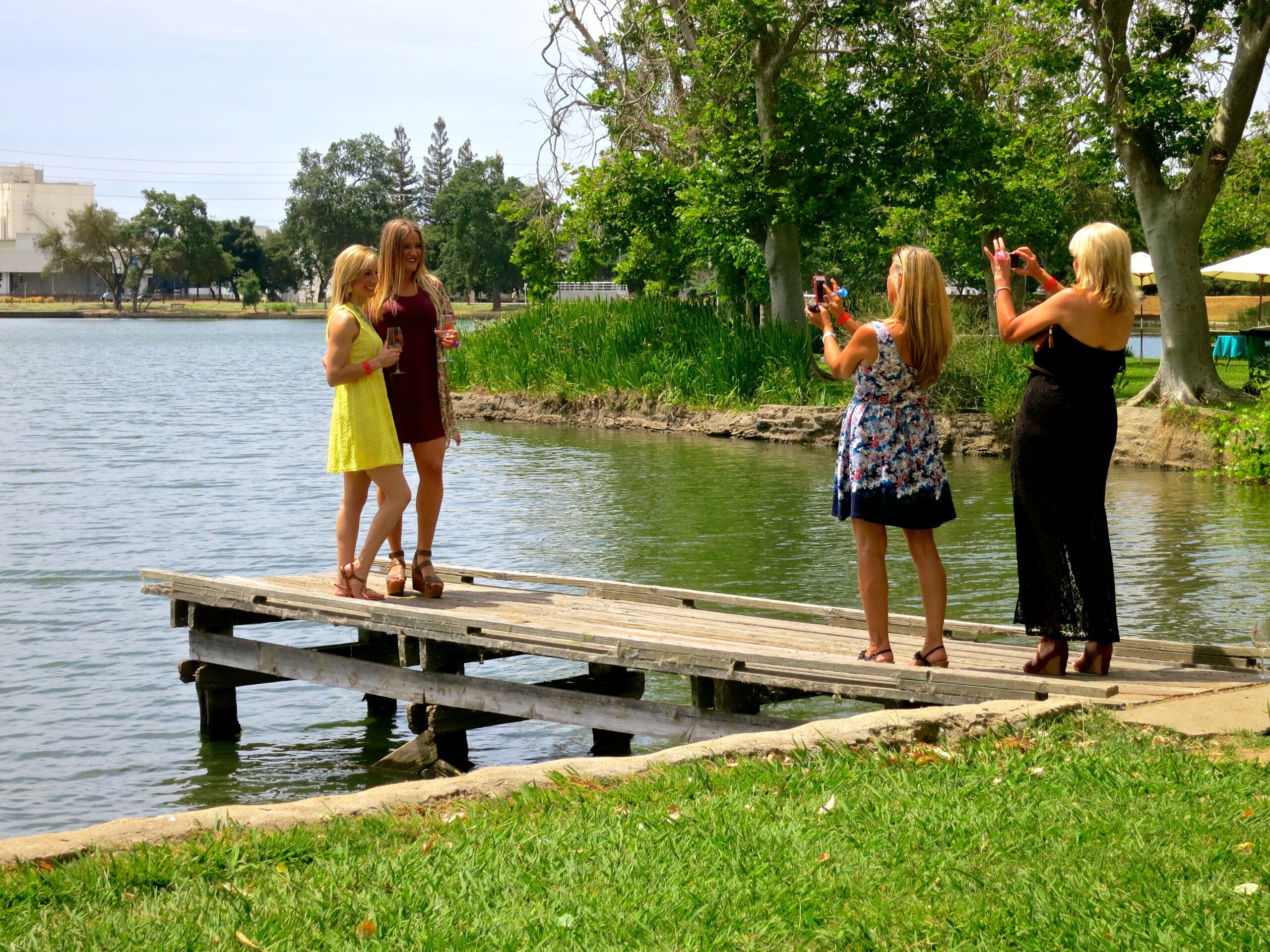 Family taking photos on a wooden dock by the water in Lodi, with trees and a park in the background.