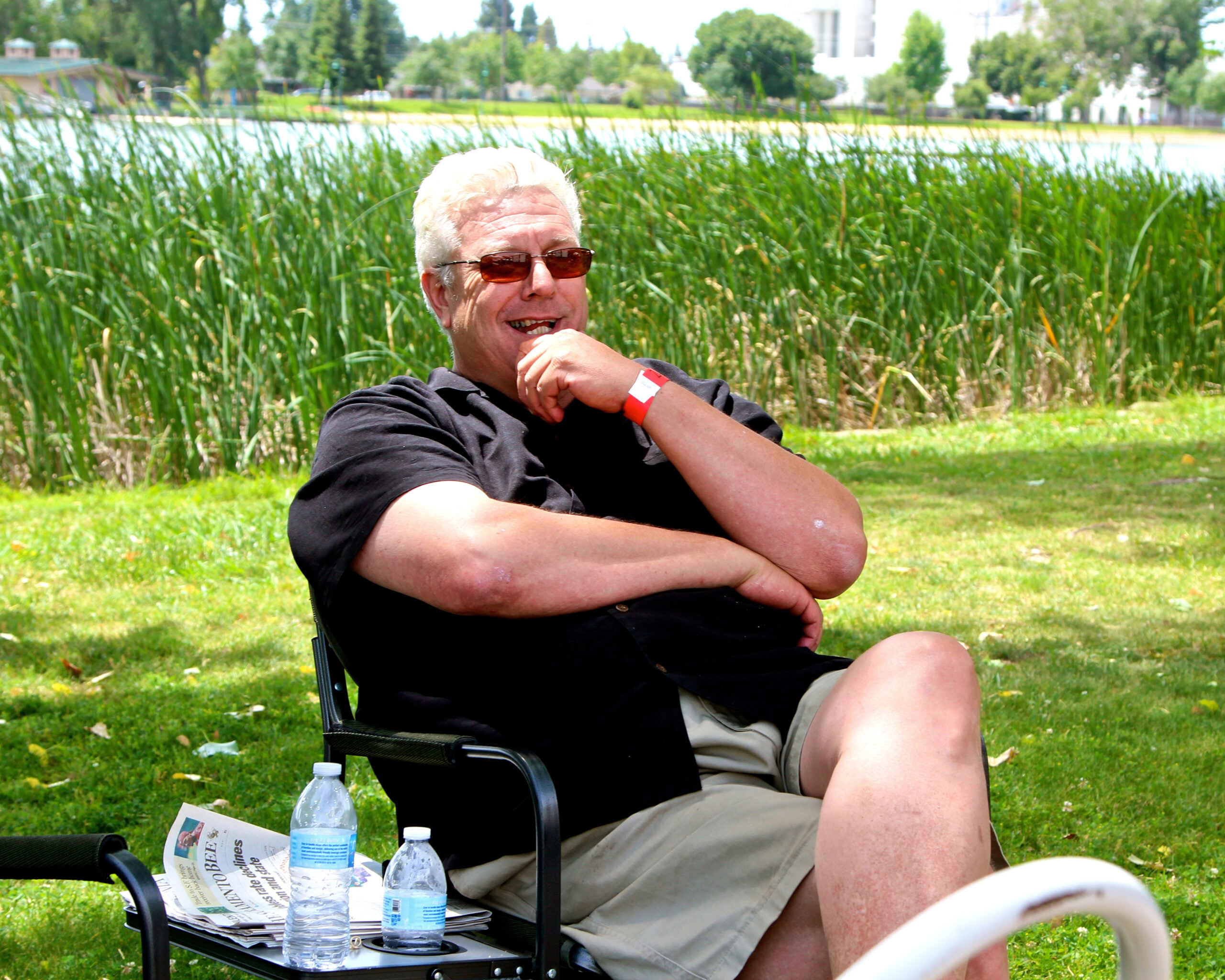 Elderly man enjoying outdoor event near a lake with wine bottles and a brochure.