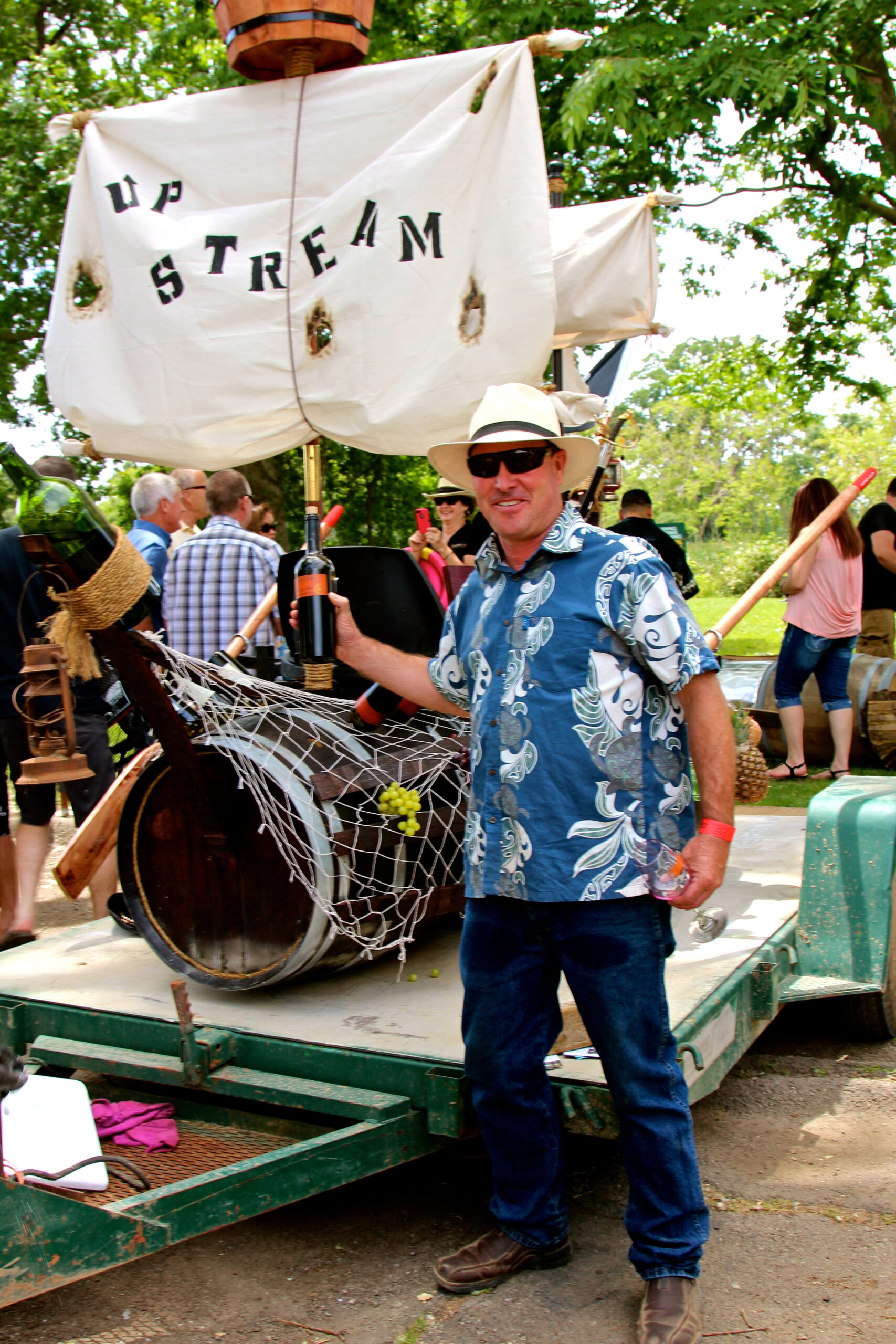 Man in Hawaiian shirt and sunglasses at Lodi wine event with boat and crowd in background.
