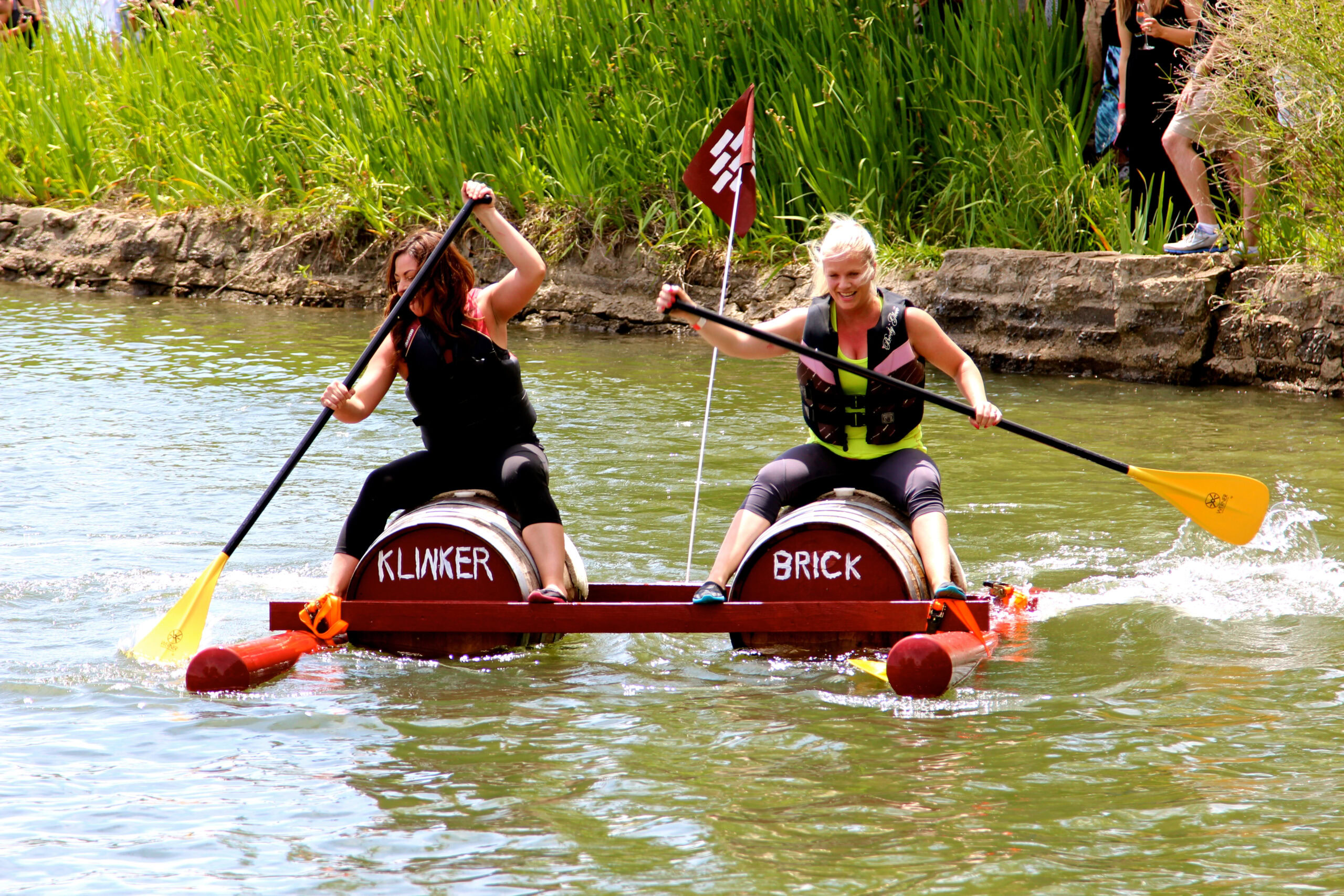 Two women paddling a raft labeled 'Klinker' and 'Brick' on a river, enjoying outdoor activity.