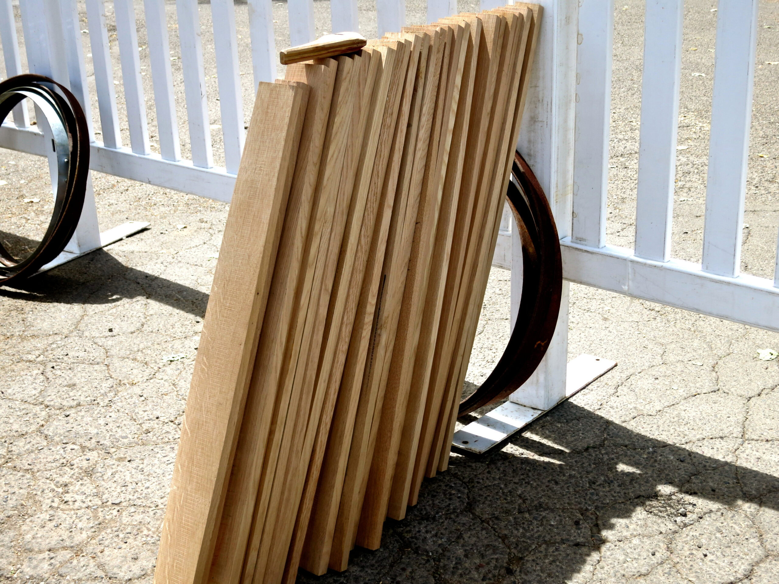 Stacked wooden folding chairs leaning against a white fence on a sunny day.