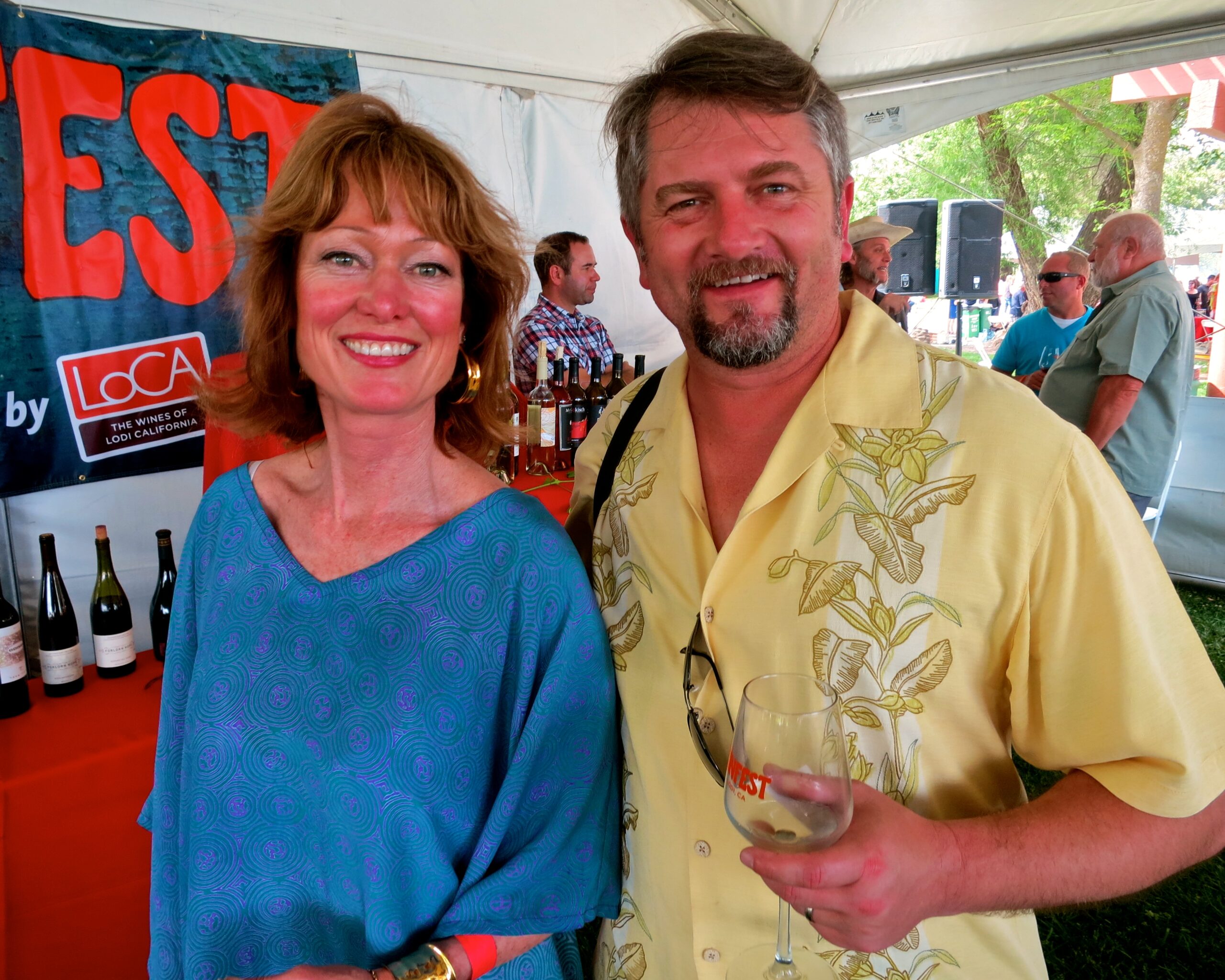 Two people enjoying wine at the Lodi Winegrape Commission event, with wine bottles in the background.