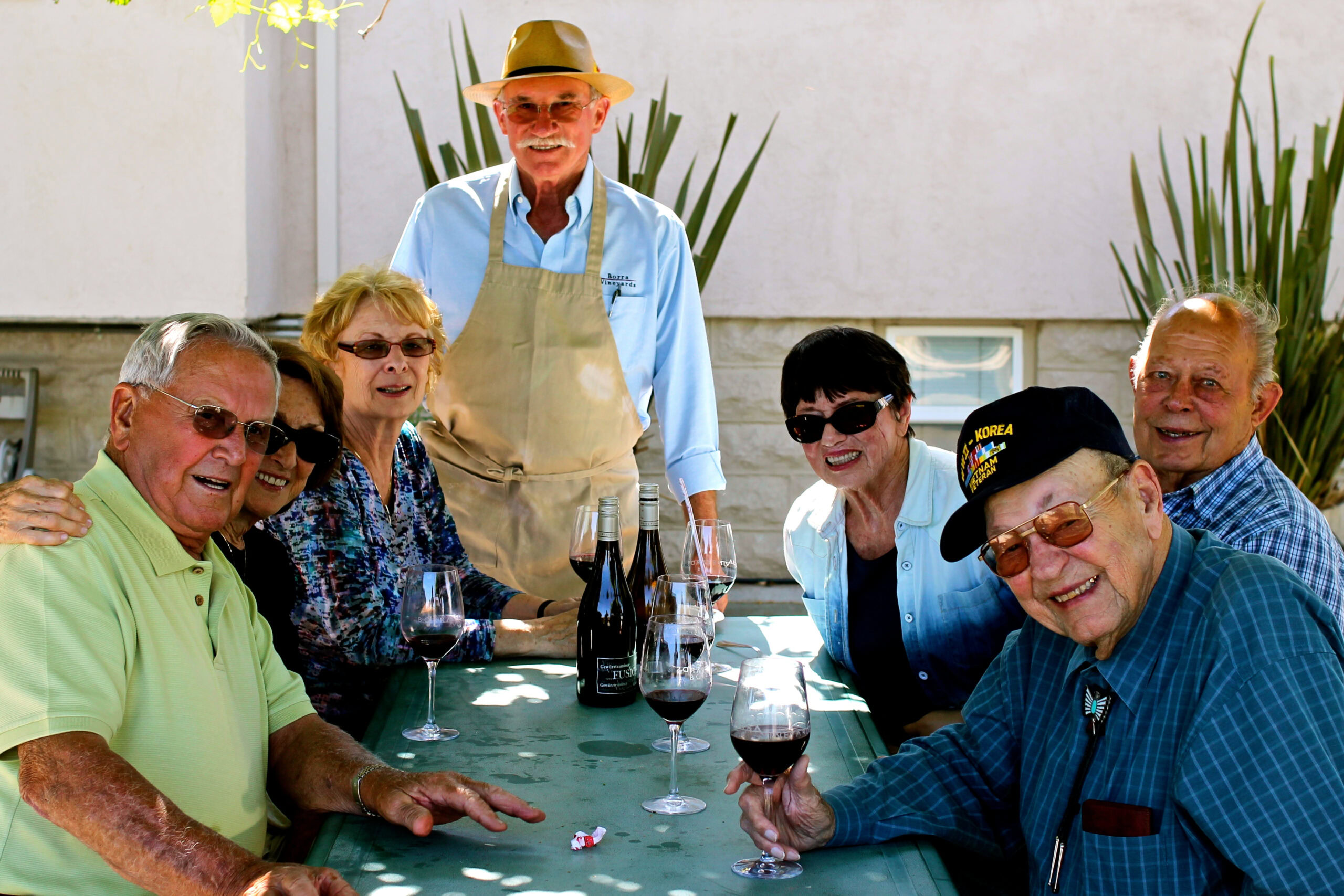 Group of seniors enjoying wine tasting outdoors, with a vineyard backdrop, representing Lodi Winegrape Commission activities.