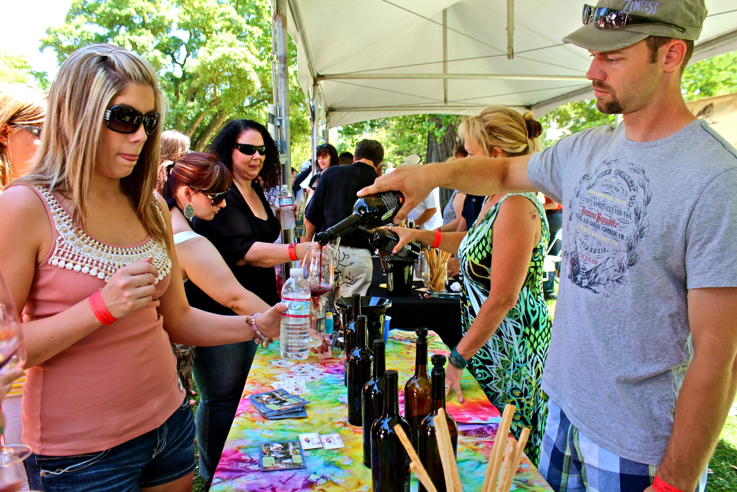 People tasting wine at a Lodi Winegrape Commission outdoor event in a park setting.