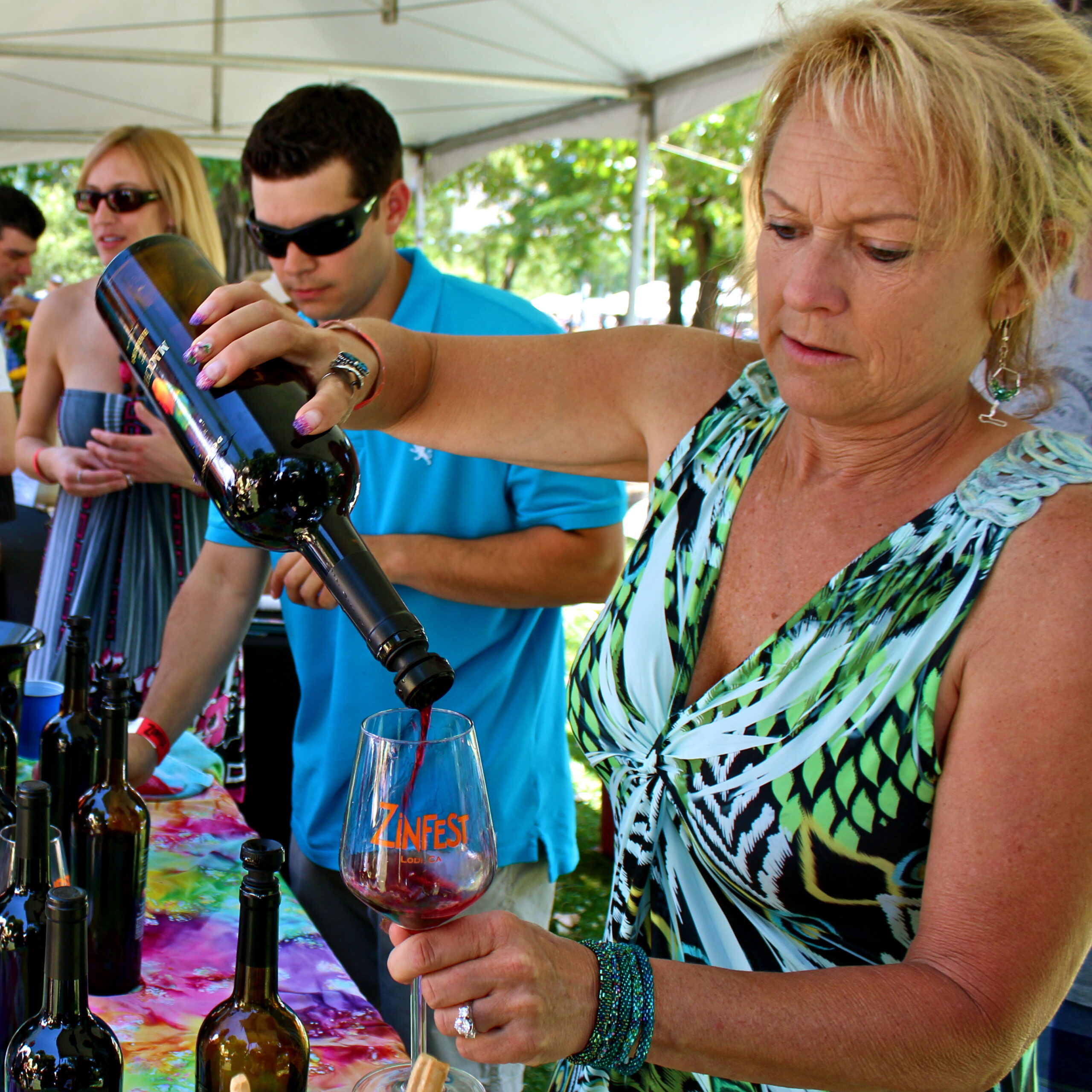 Woman pouring red wine at a Lodi wine tasting event with others in the background.