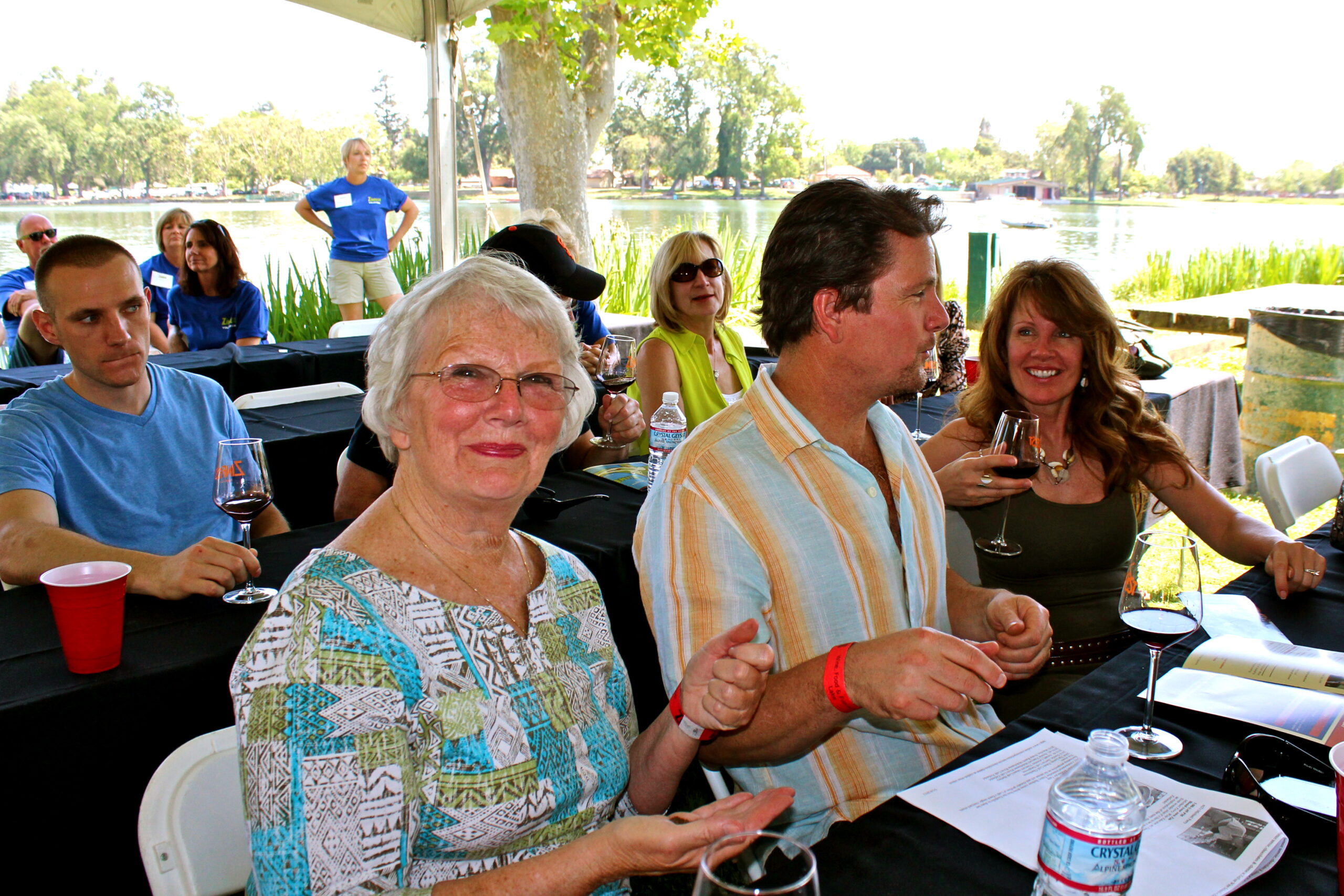 People enjoying wine tasting outdoors at a Lodi Winegrape Commission event by the lake.