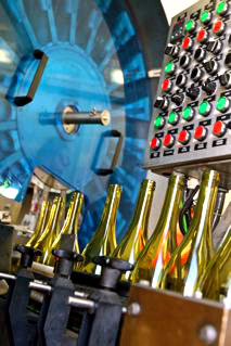 Wine bottles being filled in a modern winery with machinery and colorful control panels.