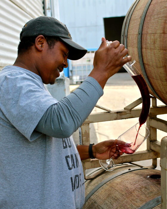 Winemaker pouring wine from barrel at Lodi Winegrape Commission facility.