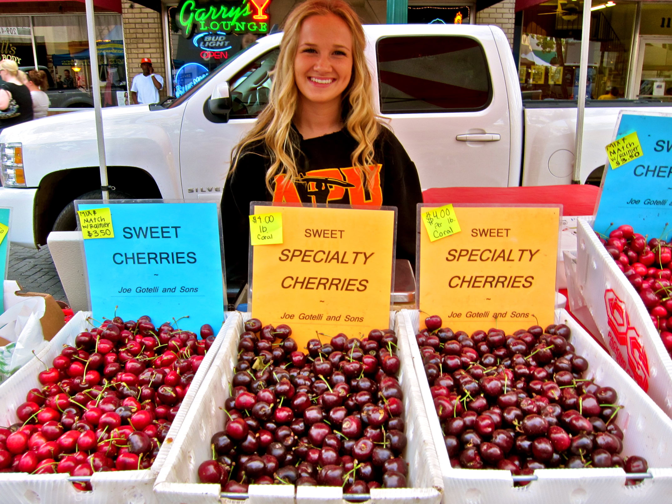 Smiling woman selling fresh cherries at Lodi Winegrape Commission market stand.