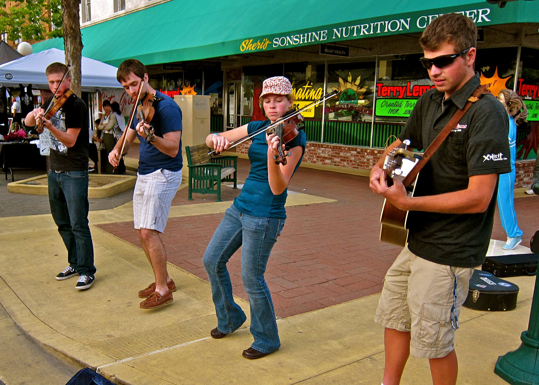 Young musicians playing violins and guitar outdoors at a street event in Lodi, California.
