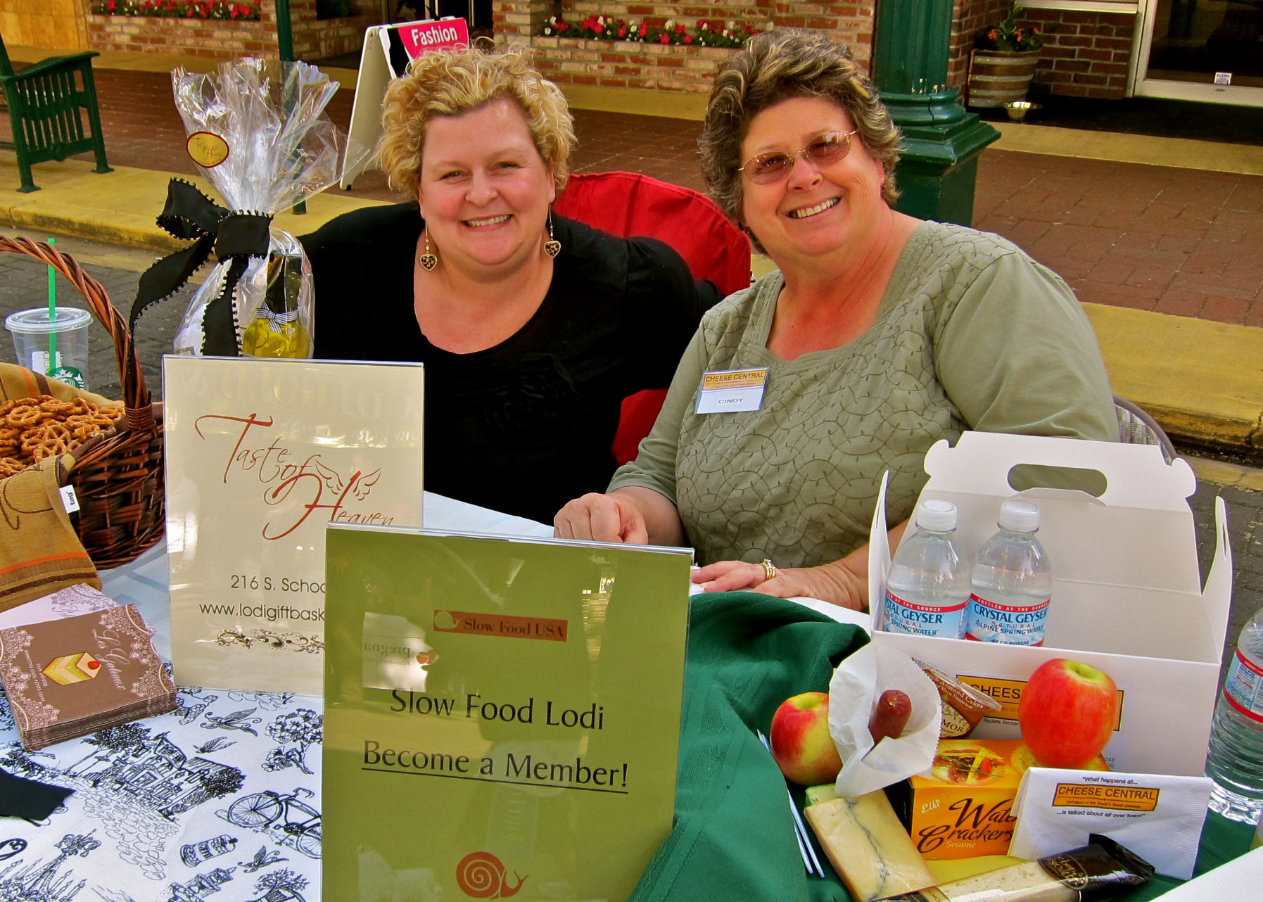 Two women smiling at a Lodi Winegrape Commission event with food and promotional materials on the table.