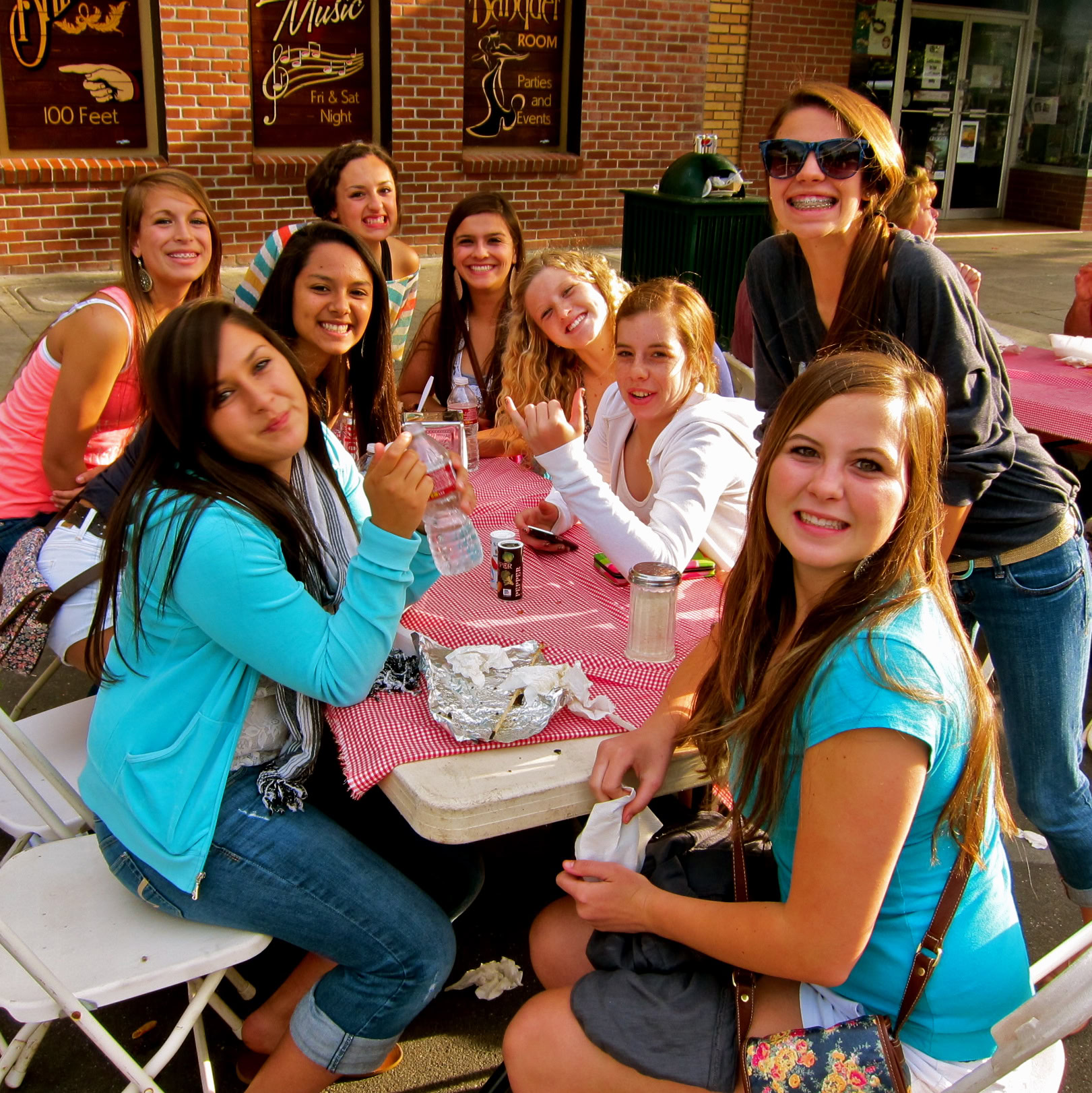 Group of young women smiling and having fun at an outdoor event with a red checkered tablecloth.
