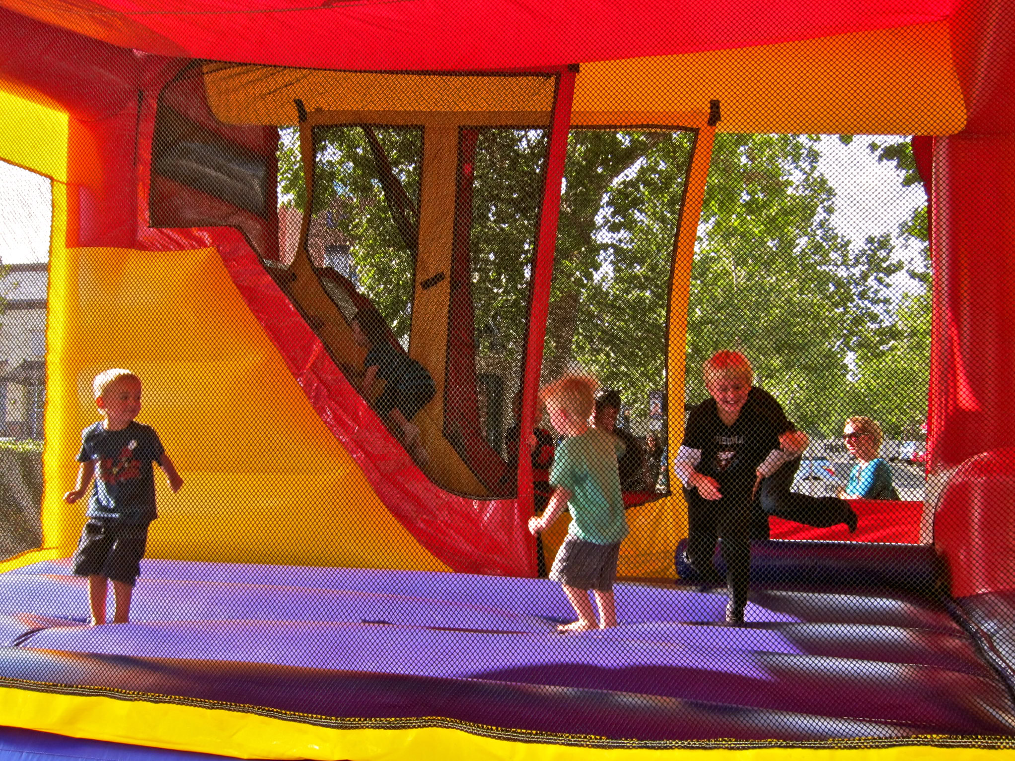 Children enjoying a bounce house at an outdoor event with trees in the background.