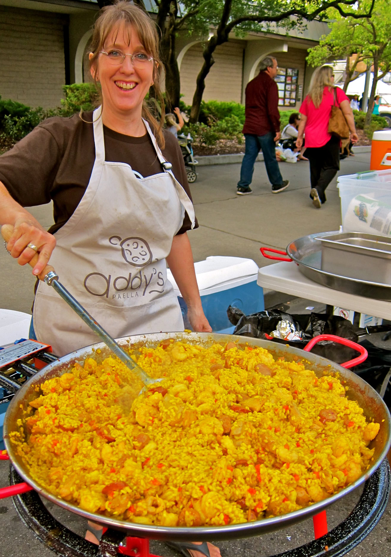 Woman cooking yellow rice dish at Lodi wine event with people in background.