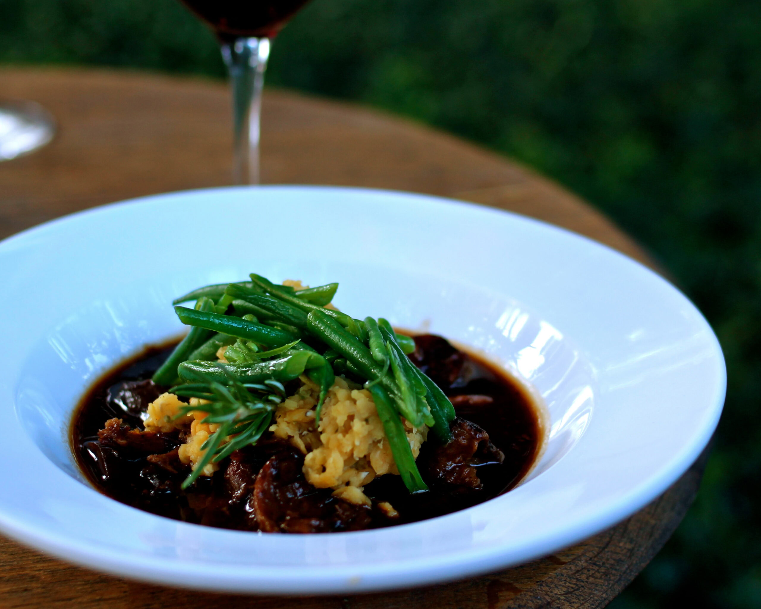 Close-up of a gourmet dish with green beans, mashed potatoes, and dark sauce on a white plate.