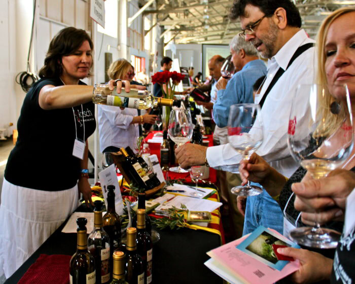 People tasting and pouring wine at a Lodi Winegrape Commission event in a bright indoor setting.