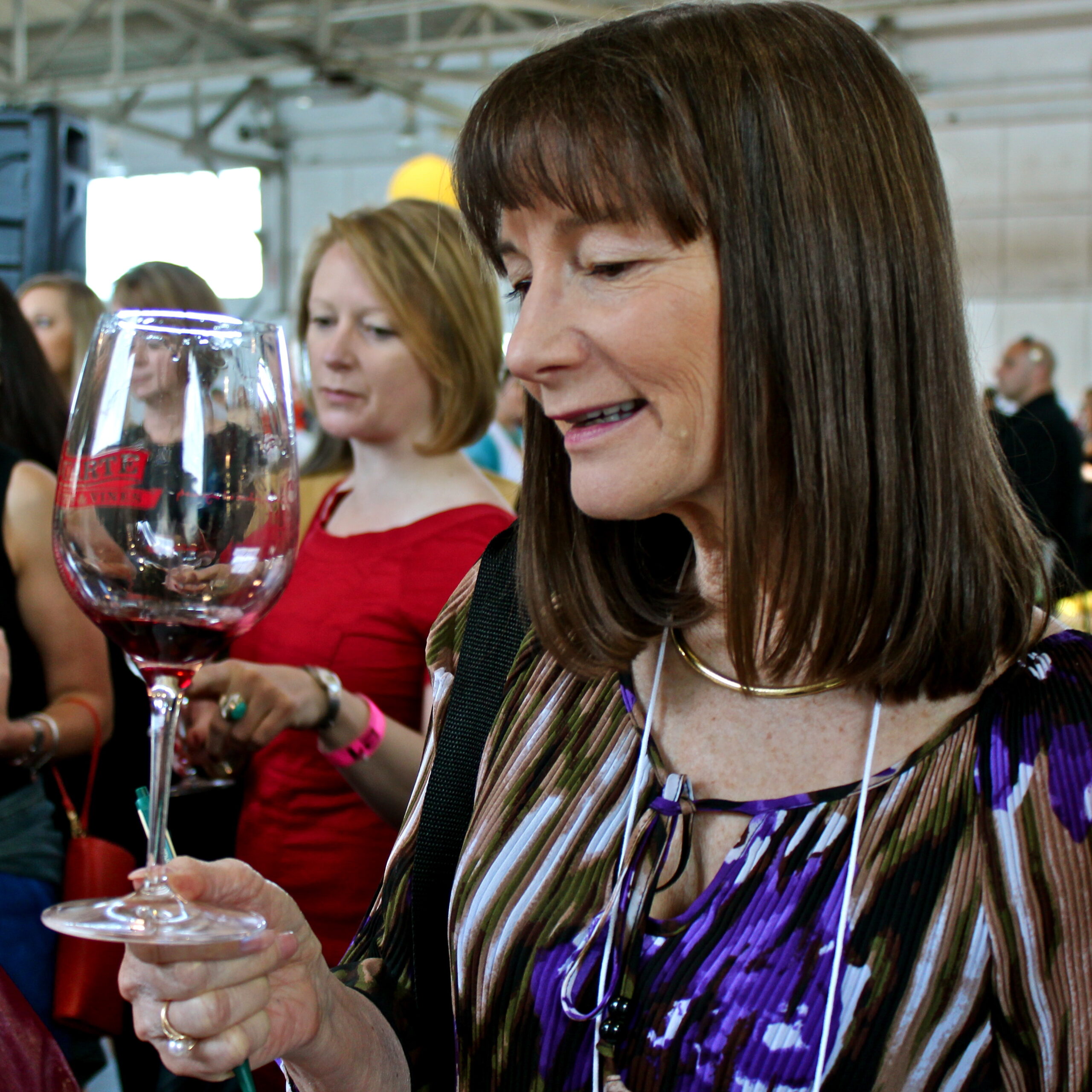 Woman examining a glass of red wine at a Lodi wine event, surrounded by attendees under a tent.