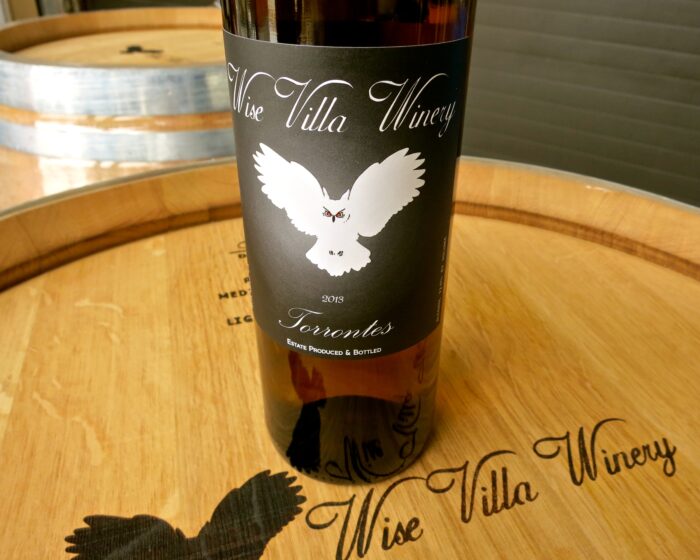Close-up of Wise Villa Winery wine bottle with owl logo on a wooden barrel.