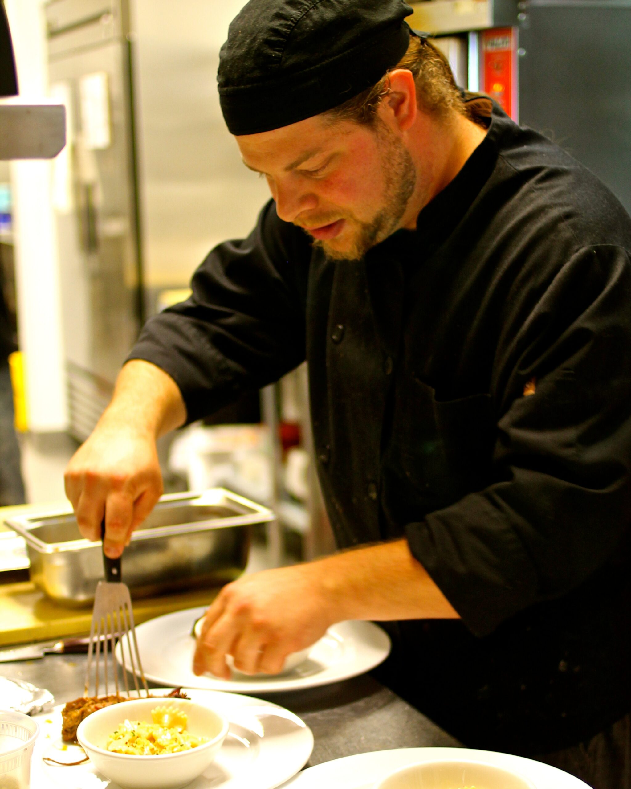 Chef in black uniform garnishing a dish in a professional kitchen for Lodi Winegrape Commission.