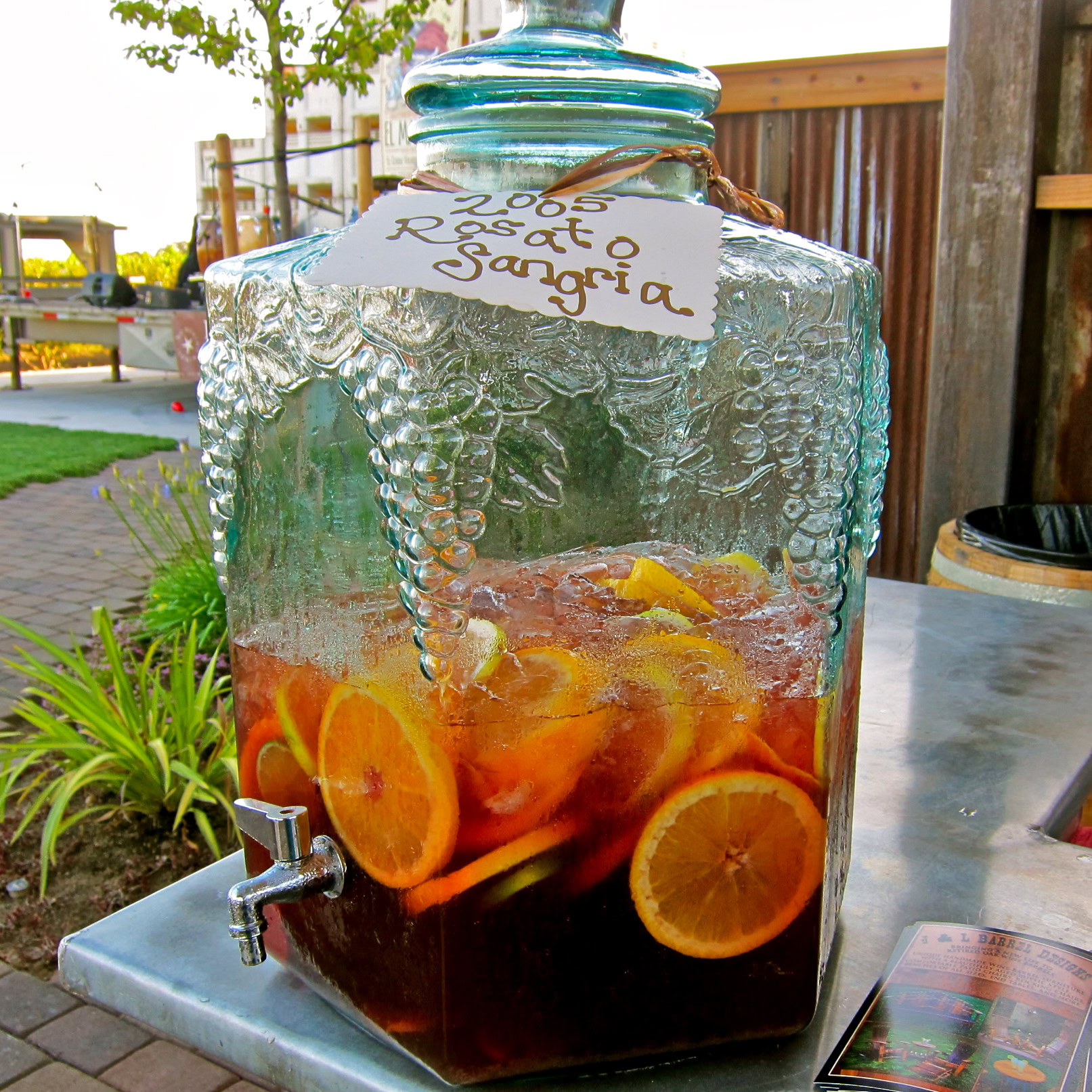 Glass beverage dispenser with lemon and orange slices, promoting Lodi winegrape region.