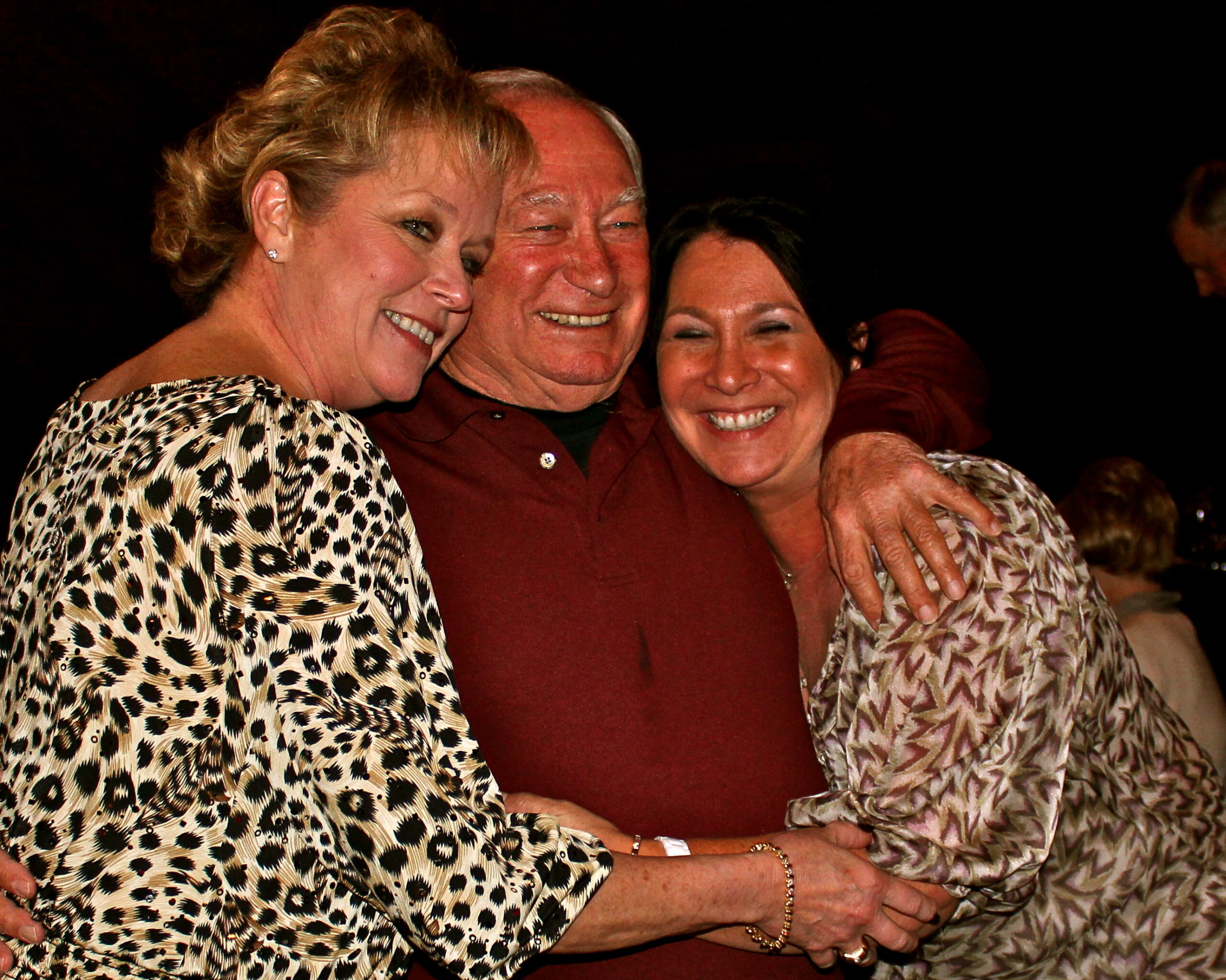 Three people smiling and hugging at a Lodi Winegrape Commission event, showcasing community and wine industry camaraderie.