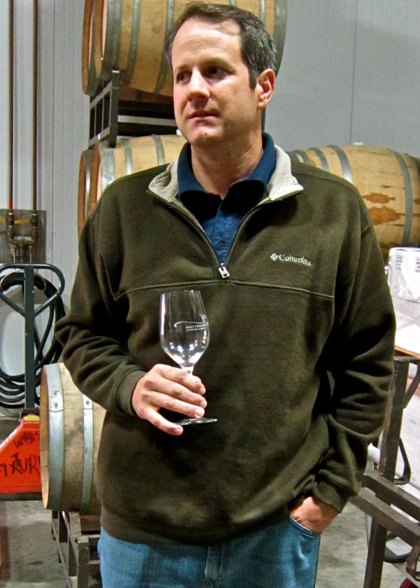 Man holding a wine glass at a Lodi wine tasting event, surrounded by wine barrels.