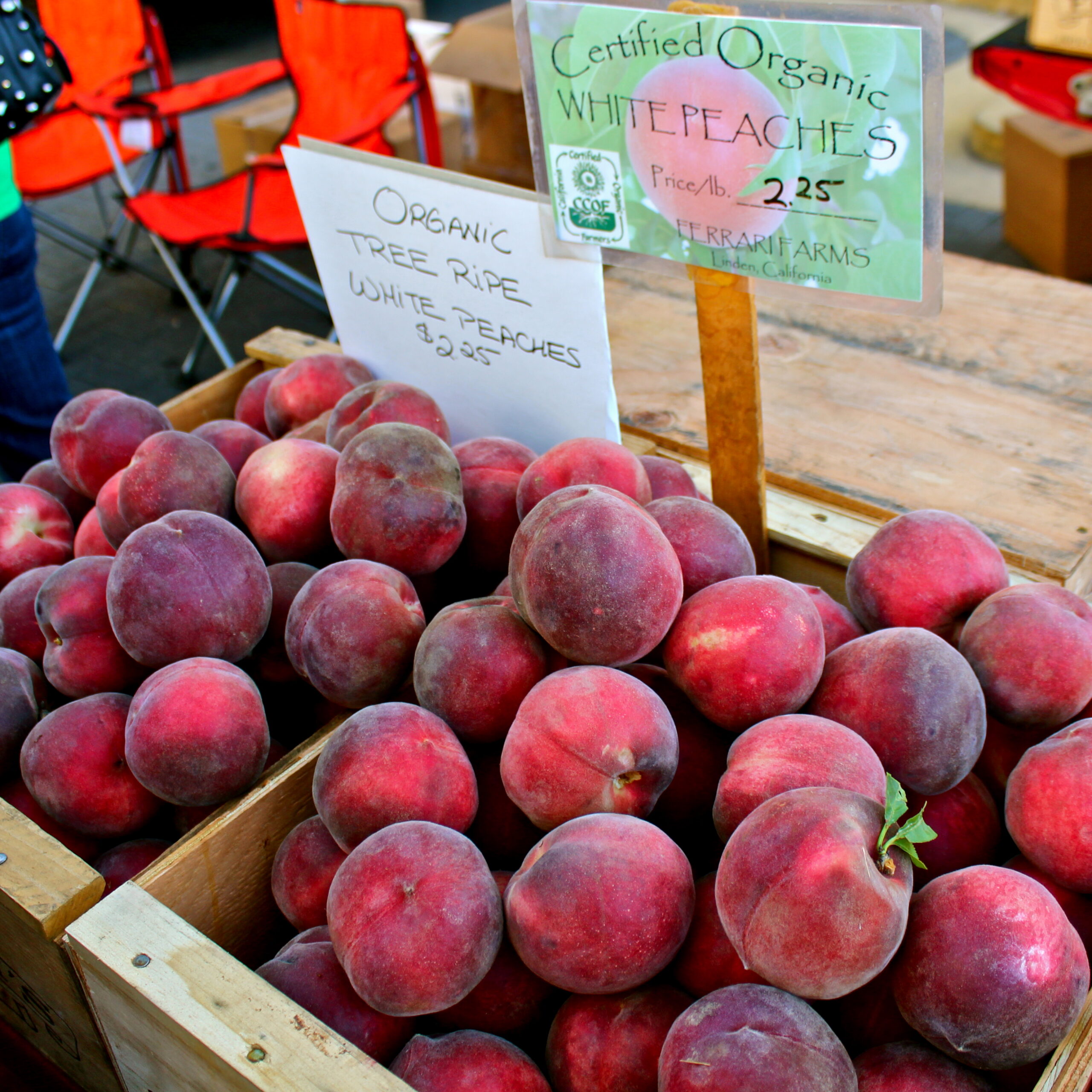 Fresh organic white peaches at Lodi market with signs indicating price and certification.