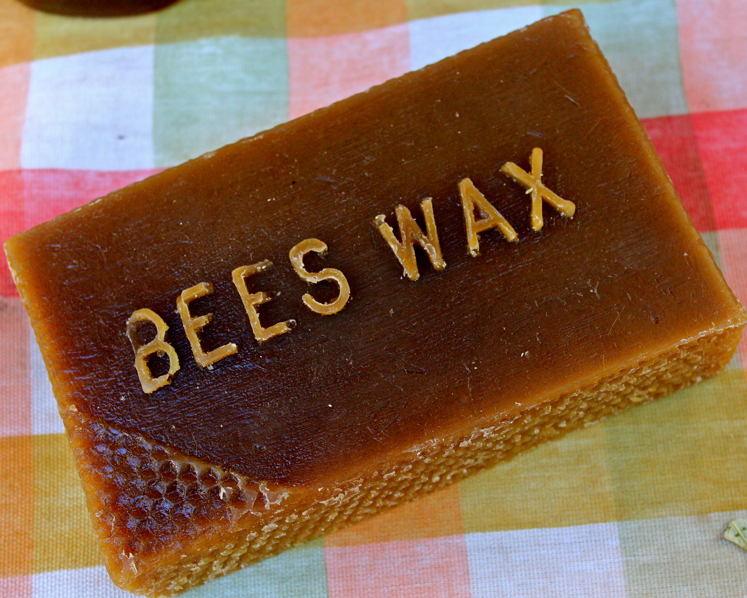 Honey block with 'BEES WAX' inscription on top, on a colorful checkered cloth background.