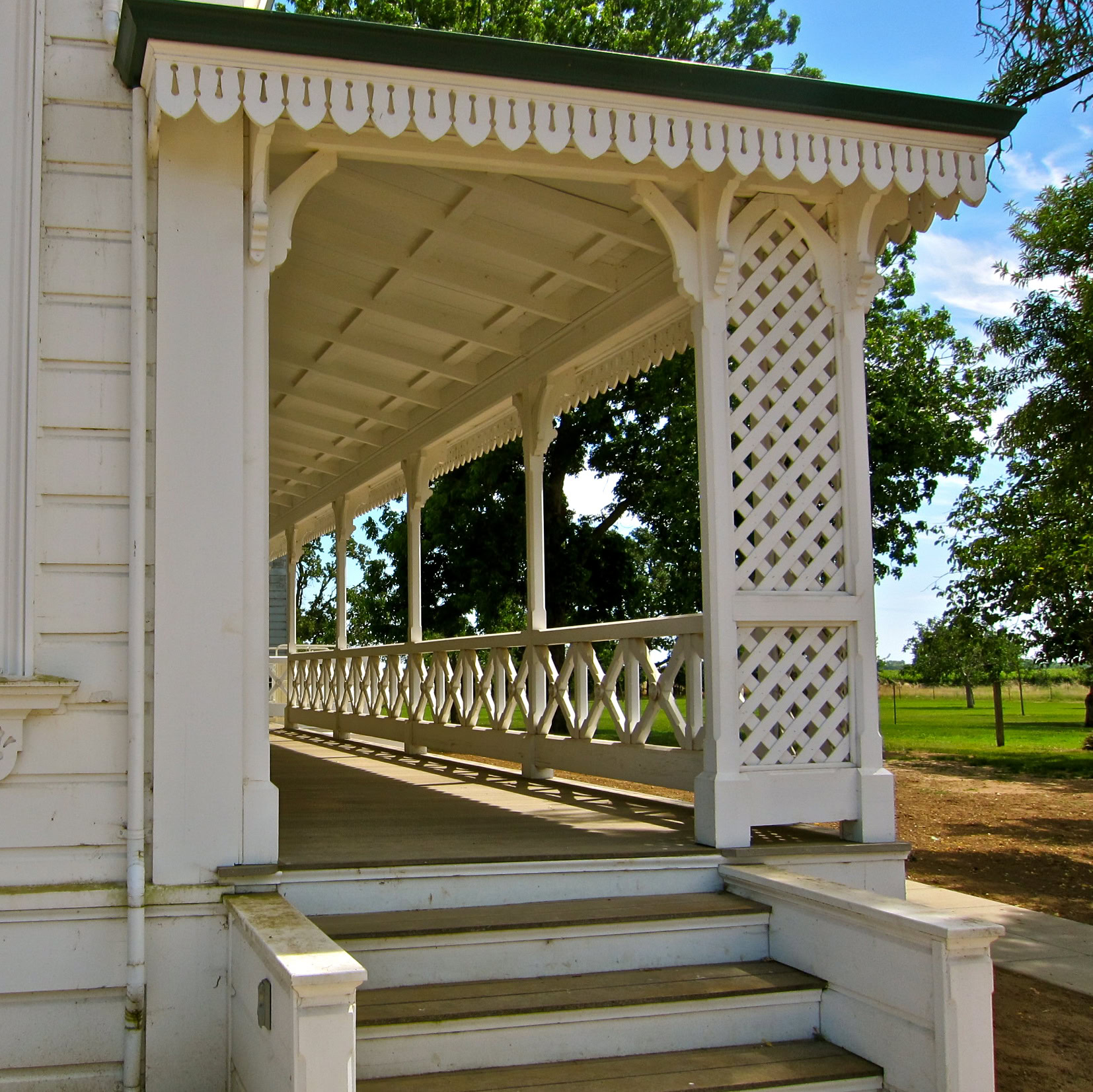 White wooden pavilion with decorative lattice and steps in a lush vineyard setting in Lodi, California.