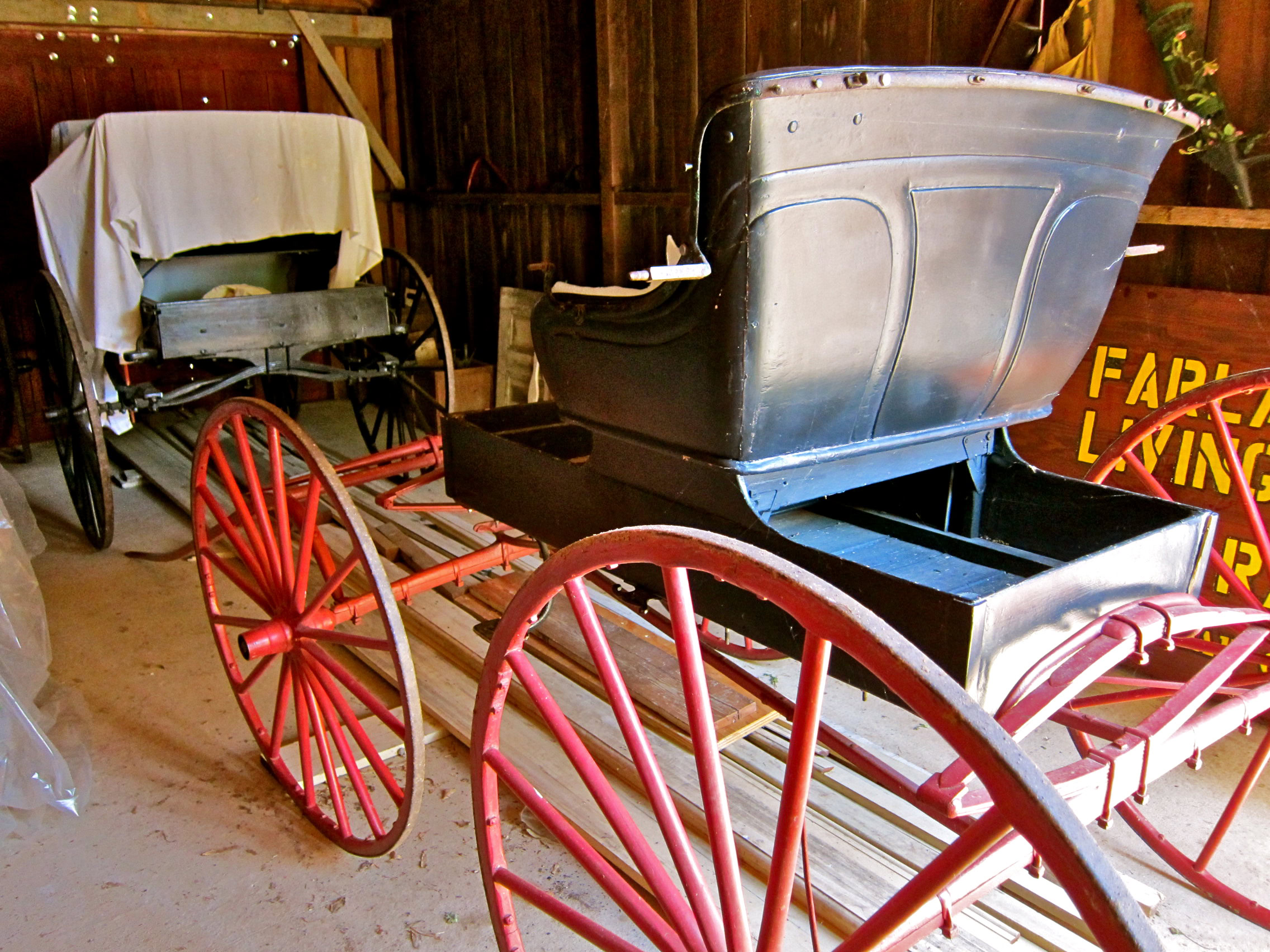 Antique horse-drawn carriage with red wheels in a rustic setting, showcasing historical transportation.