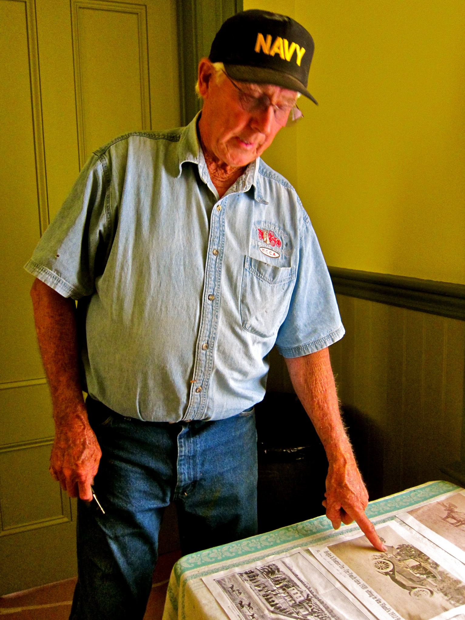 Elderly man in Navy cap and denim shirt pointing at winegrape map.