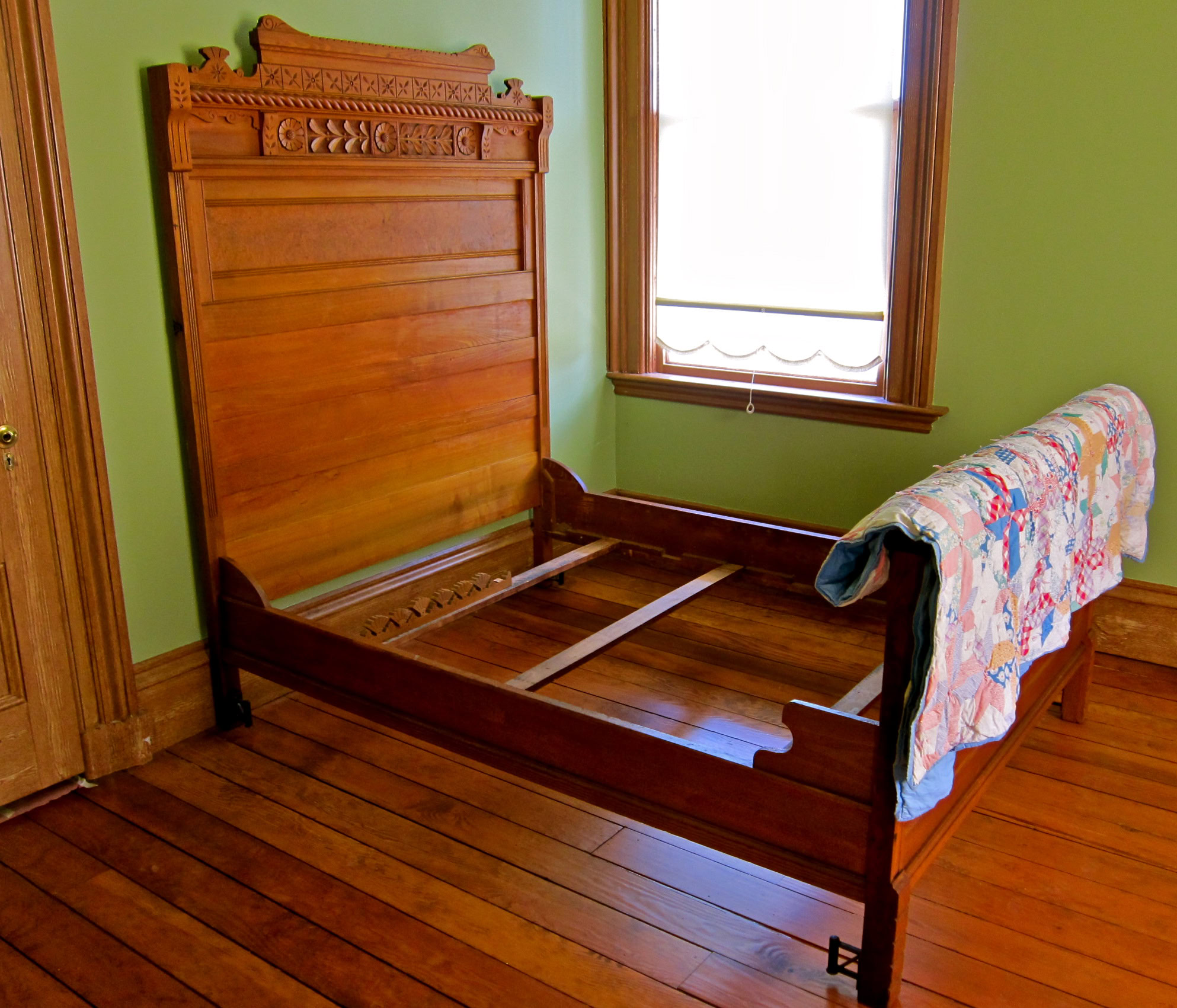 Antique wooden bed frame with intricate headboard design in a room with green walls and hardwood floors.