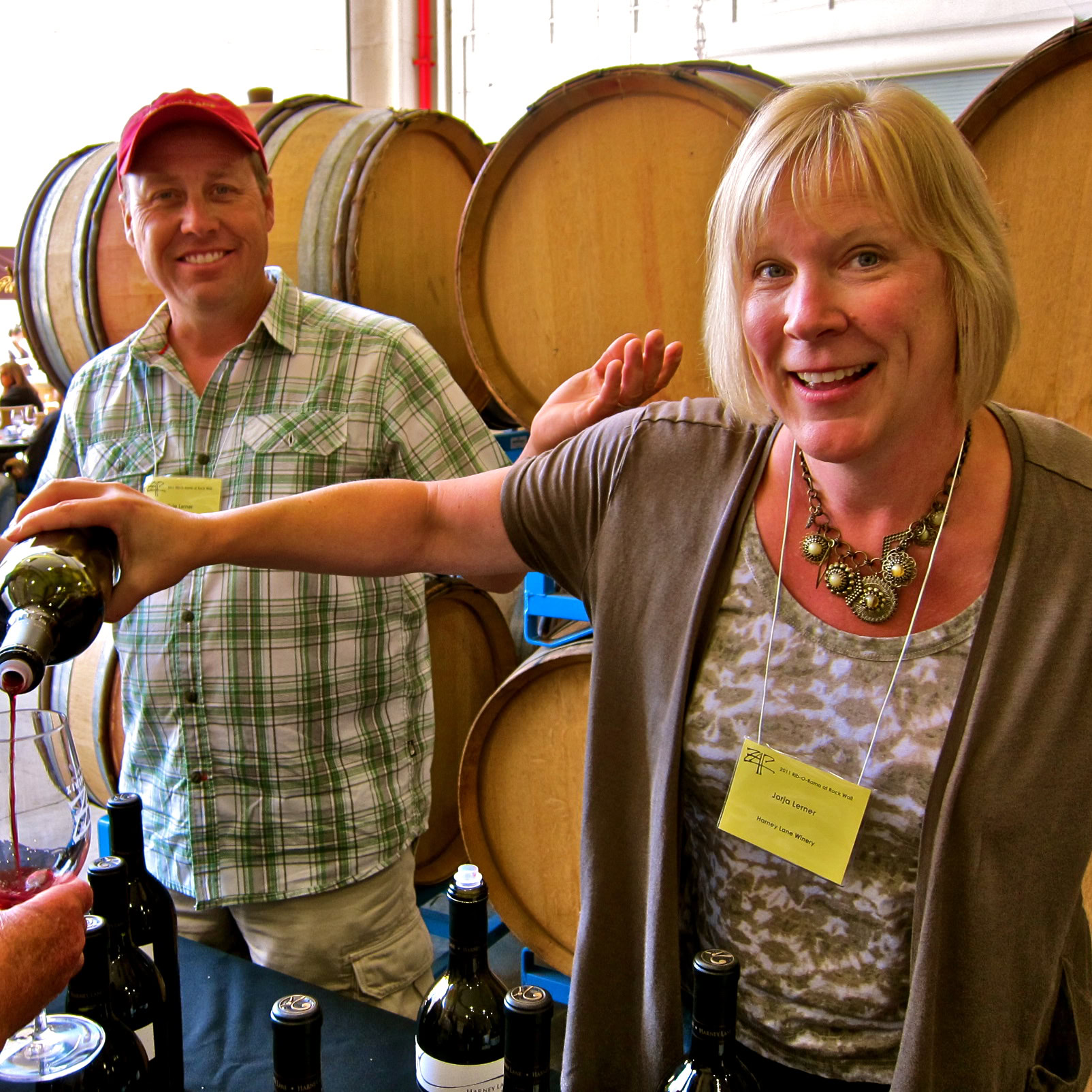 People tasting wine at a Lodi Winegrape Commission event with wine barrels in the background.