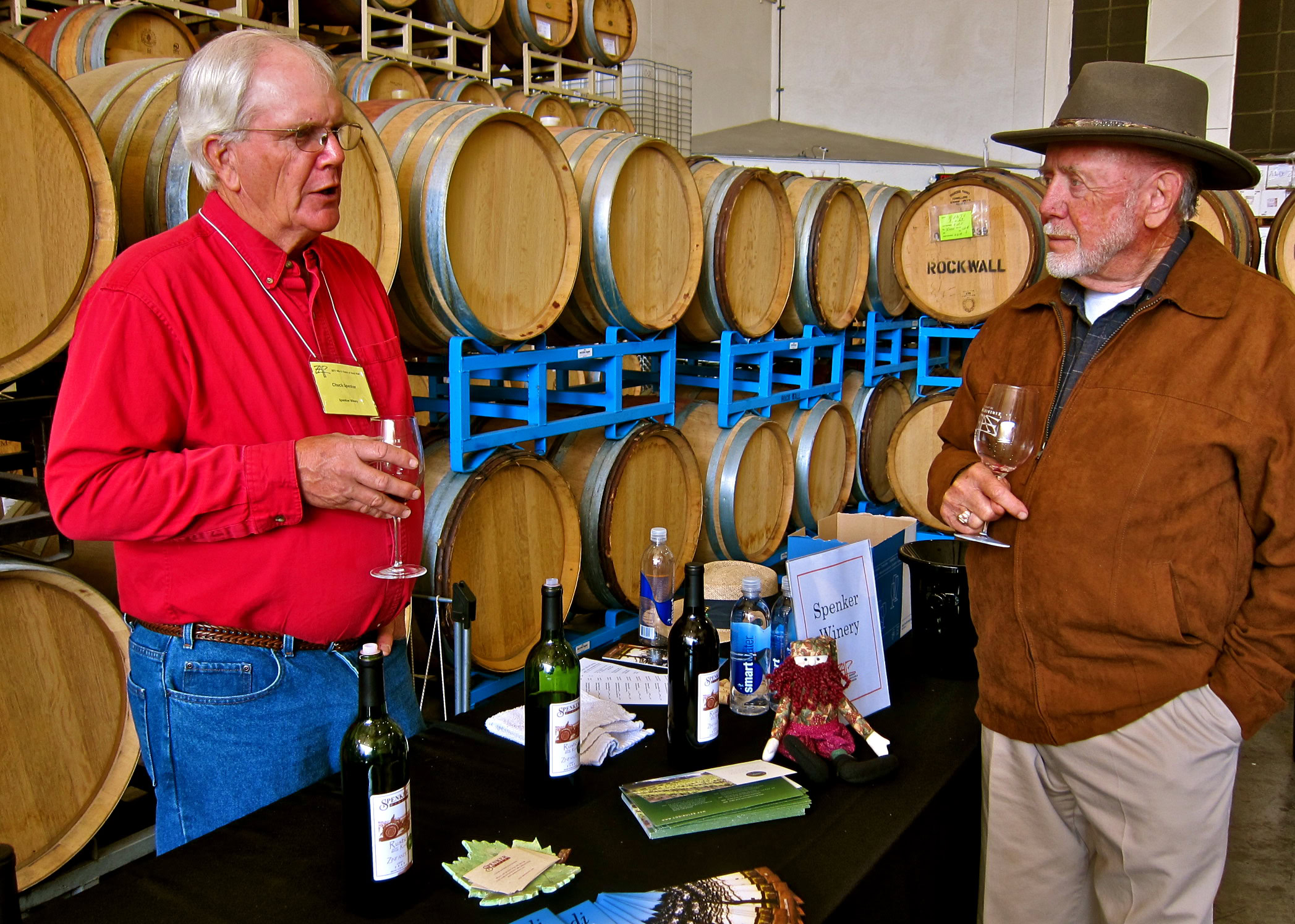 Two men tasting wine at a Lodi wine event, with wine barrels in the background.