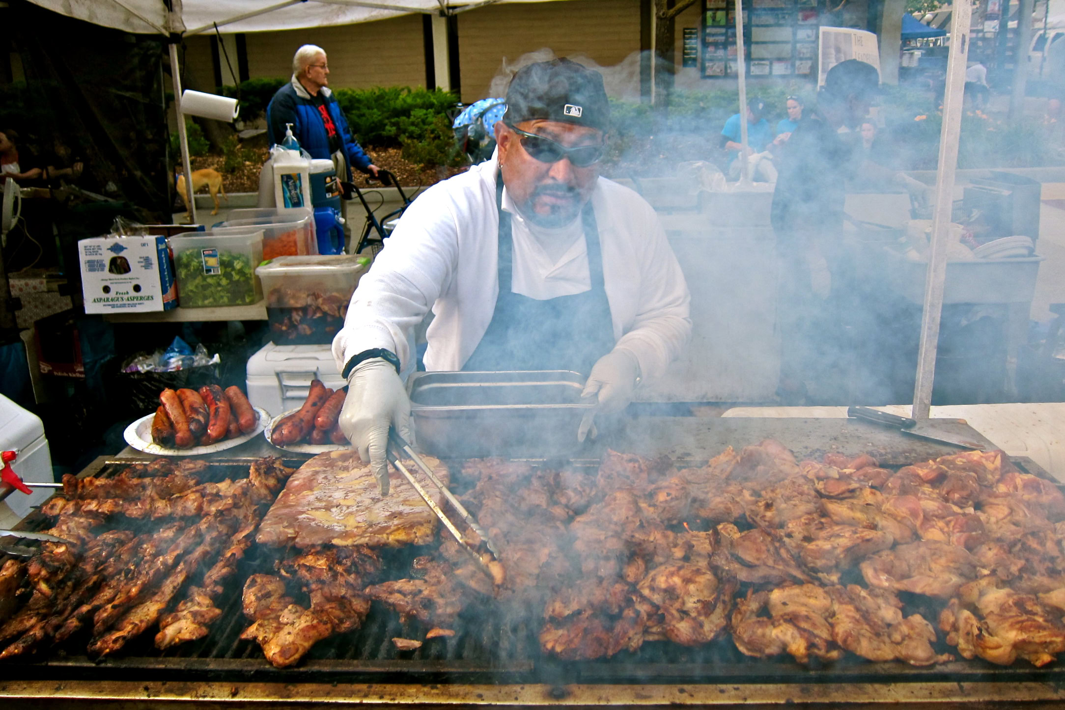 Chef grilling large cuts of meat at a Lodi wine event with smoke and outdoor setting.
