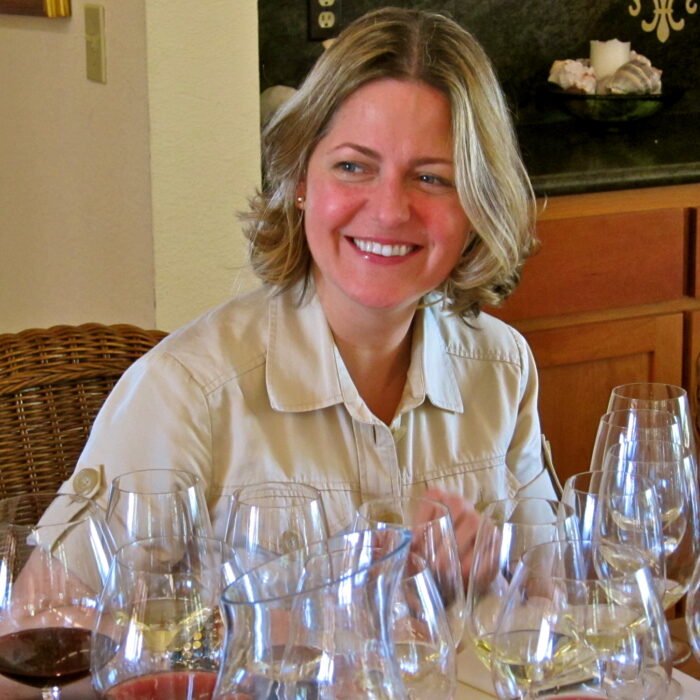 Smiling woman at wine tasting with multiple wine glasses in front of her.