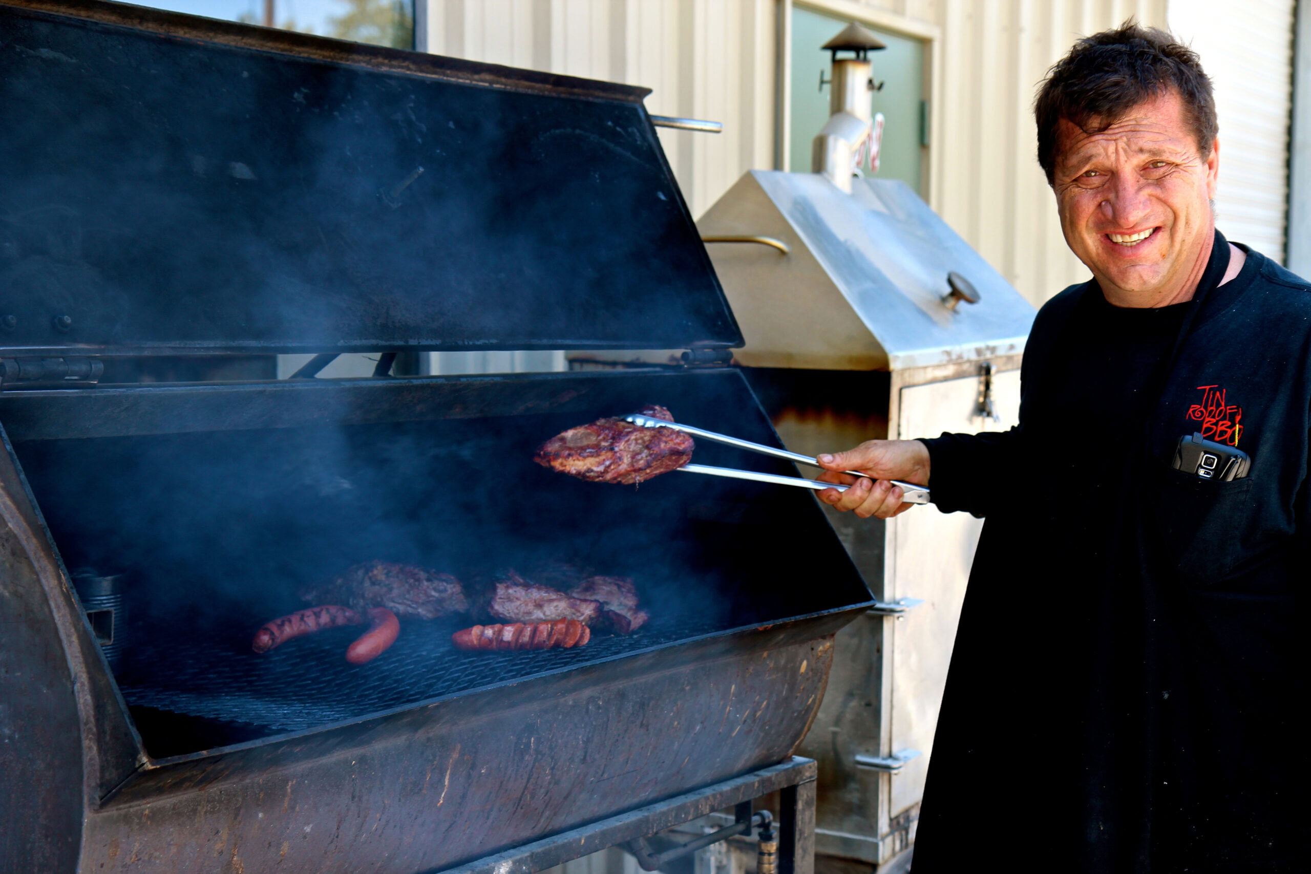 Man grilling sausages and burgers on a large outdoor barbecue grill at Lodi Winegrape Commission event.