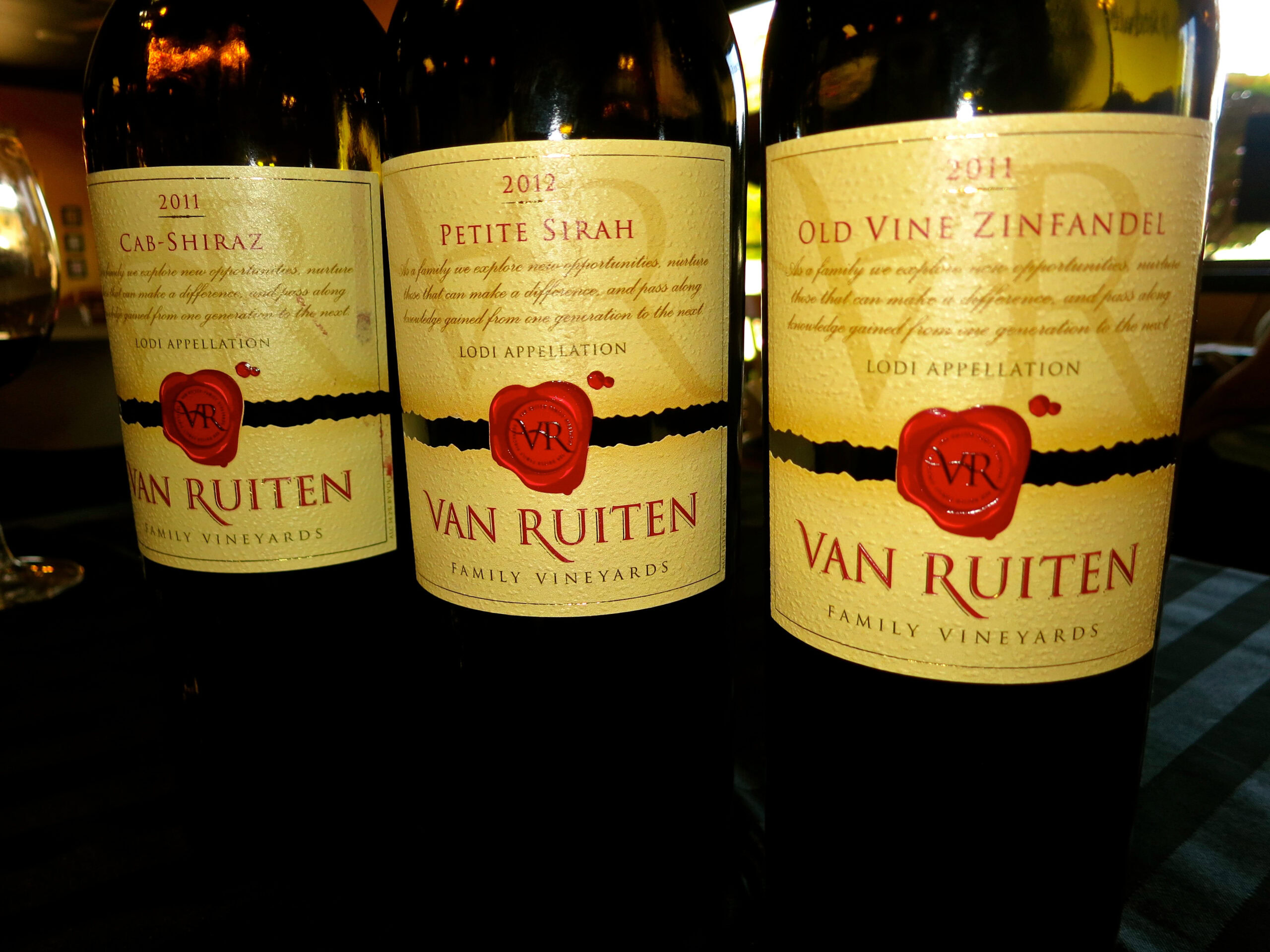Three bottles of Van Ruiten wine from Lodi Winegrape Commission, showcasing different varietals and vintages.