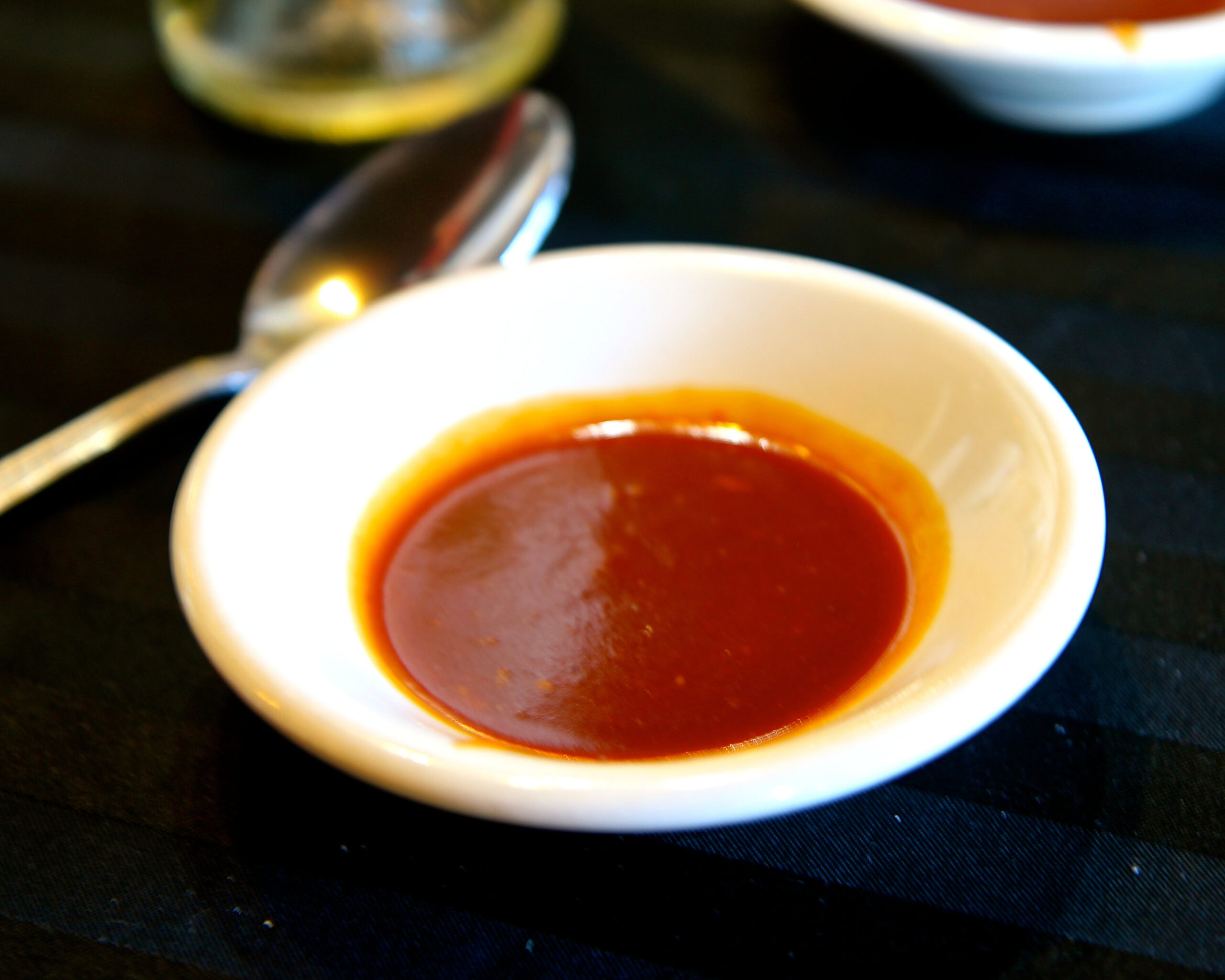 Small white bowl of red wine sauce on a black table with spoon and lemon in background.