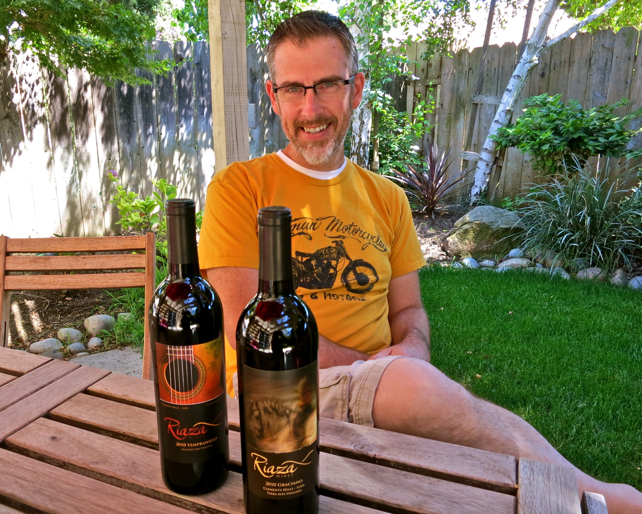 Man enjoying wine outdoors with two bottles of Lodi wine on a wooden table.