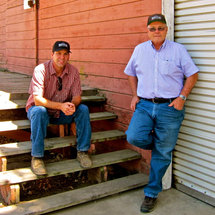 Two men from the Lodi Winegrape Commission posing outdoors near a red wooden building.