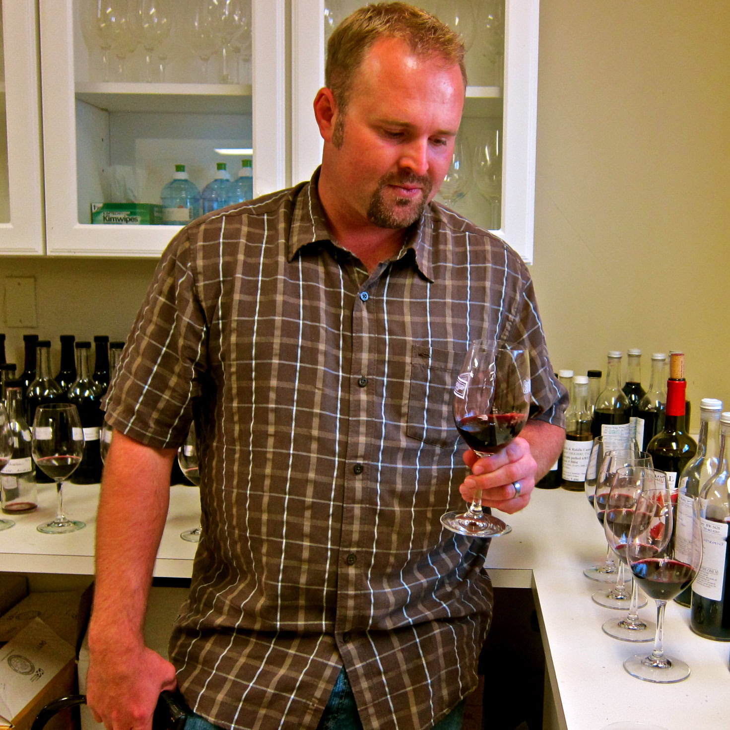 Man tasting red wine at Lodi Winegrape Commission event with wine bottles in background.