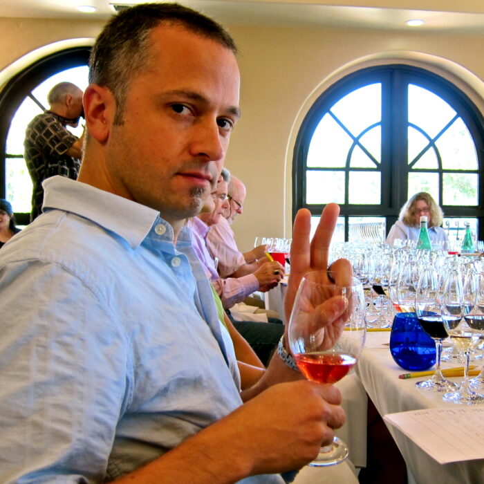 Man at wine tasting event holding a glass of rosé wine and making a peace sign.