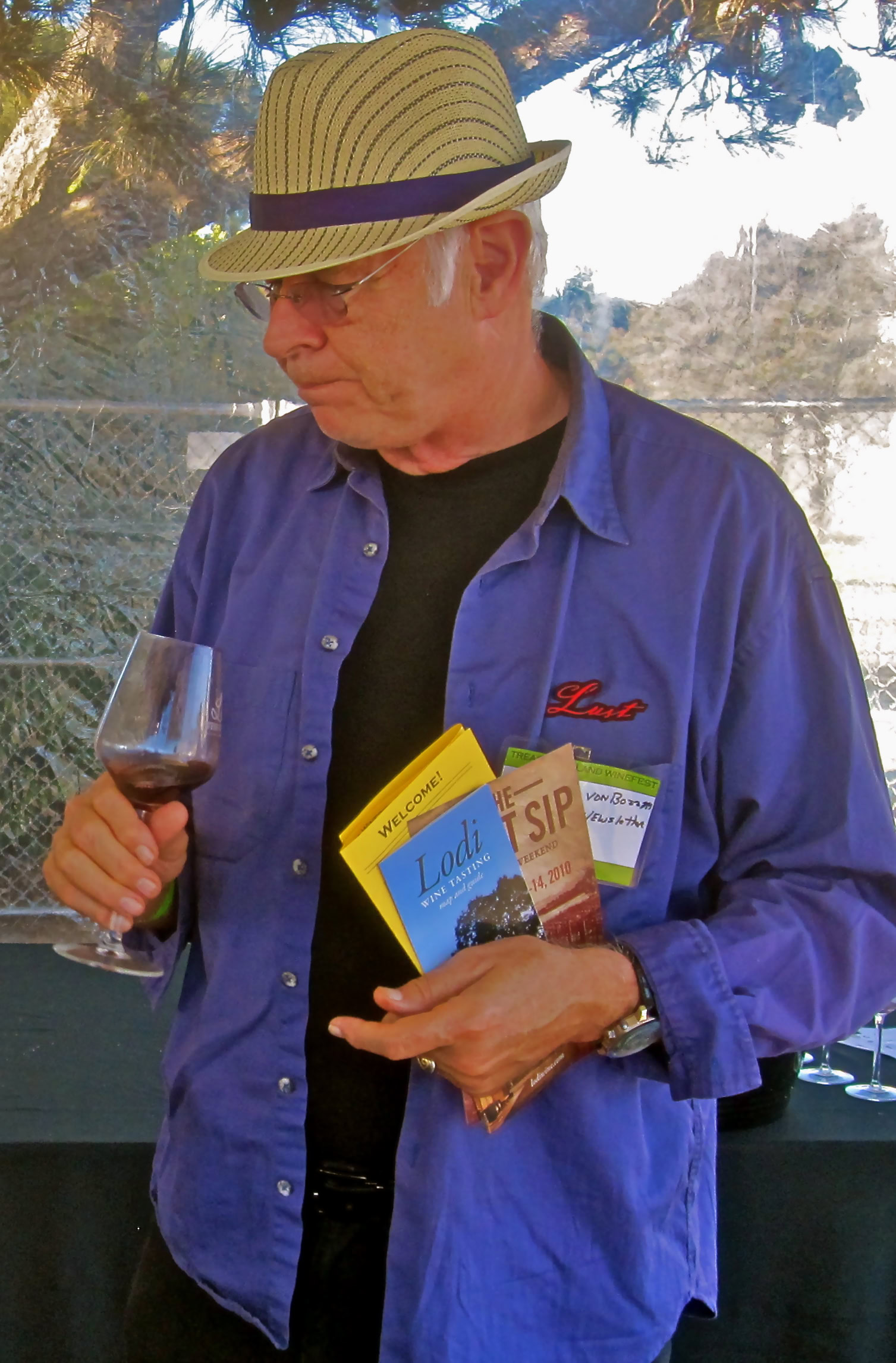 Man tasting wine at Lodi Winegrape Commission event, holding brochures and a glass of red wine.