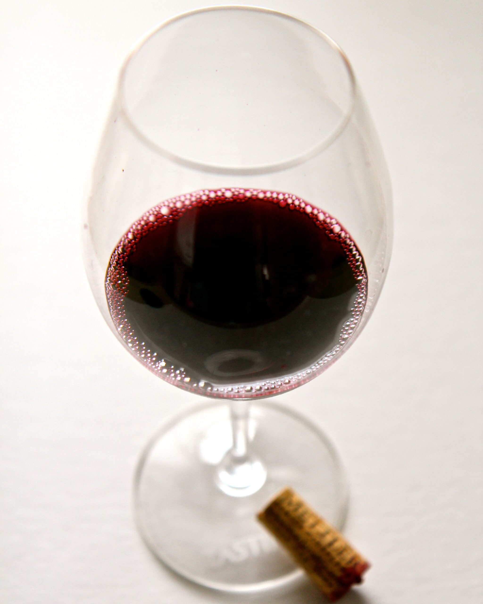 Close-up of a glass of red wine with a cork at the base, highlighting wine quality and vineyard connection.