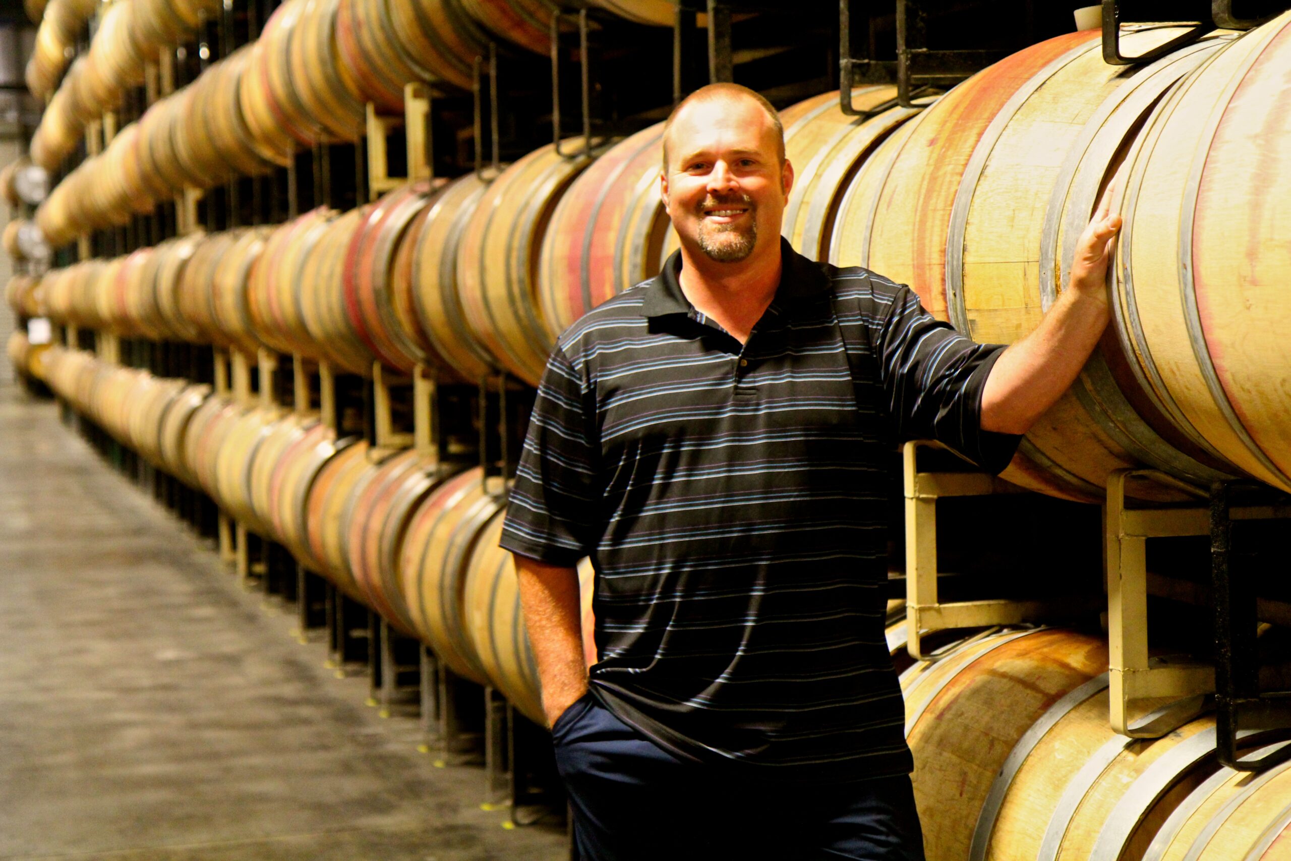Man standing in wine cellar with stacked wine barrels at Lodi Winegrape Commission.