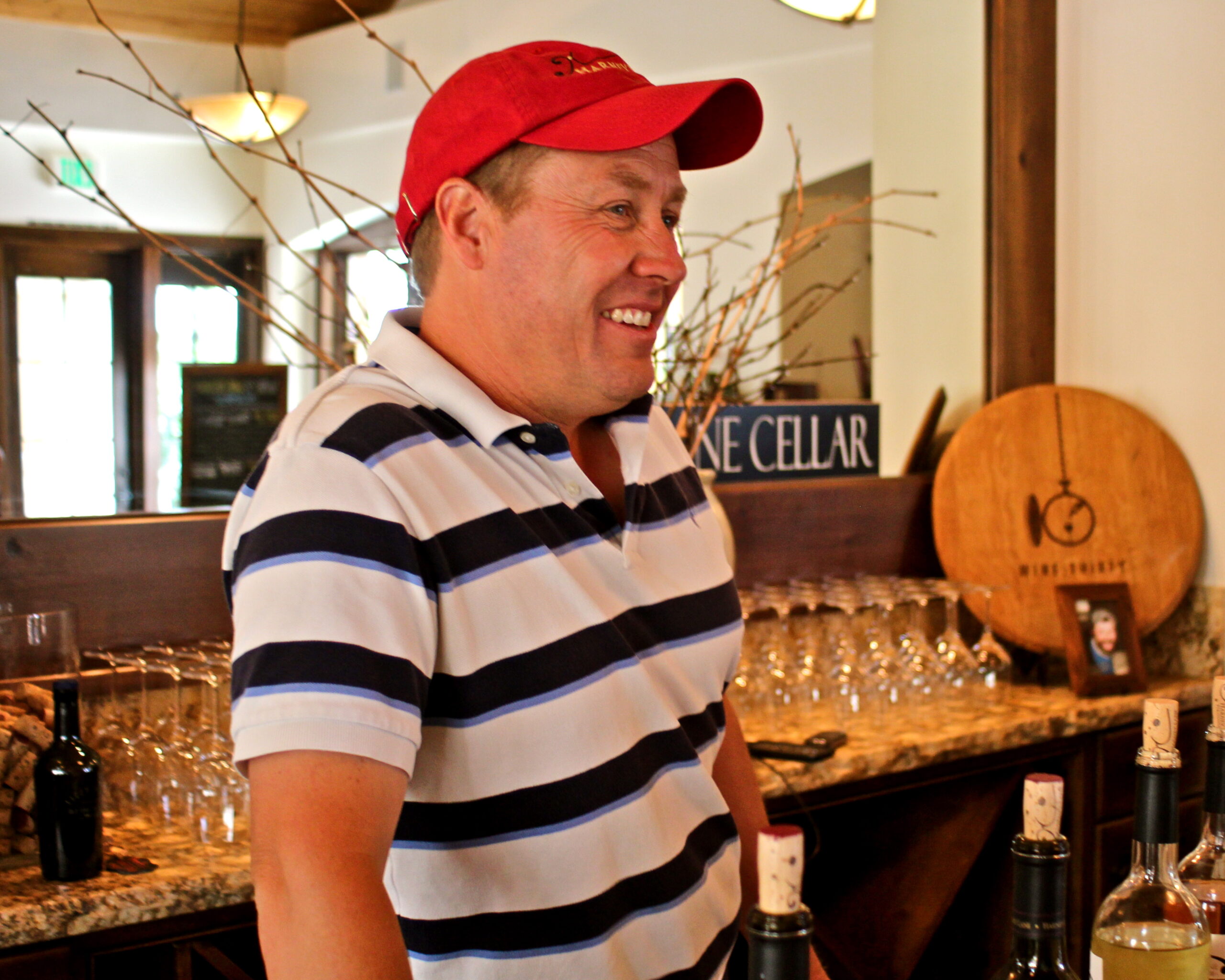 Smiling man in striped polo shirt and red cap at Lodi wine tasting event.